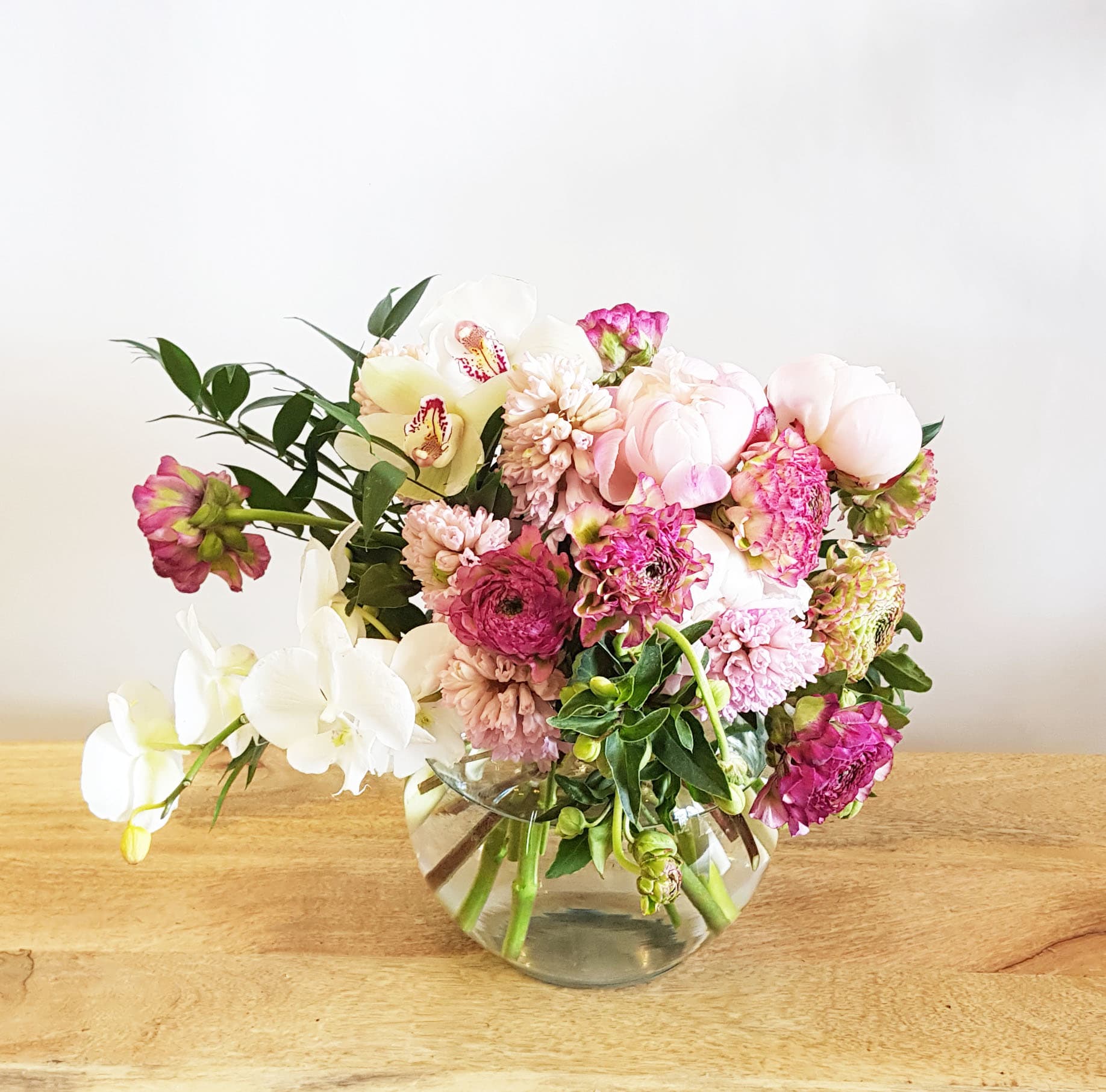 Love me tender - Exquisite peonies, ranunculus and orchids steal the show in this vibrant arrangement. Shades of fuchsia, white and pink flowers burst out of a  glass vase. Romantic and nontraditional at once, perfect for the love of your life. 