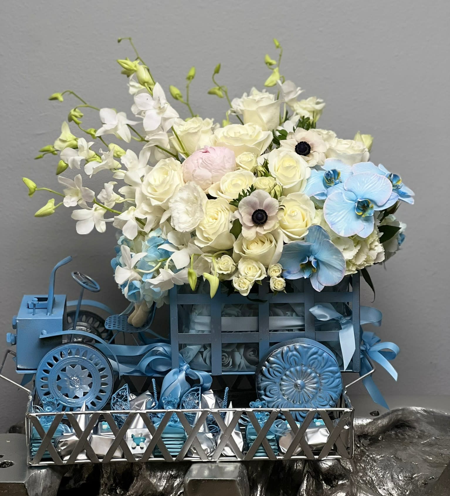 Baby Car with KV Chocolates Baby Car with KV Chocolates - A flower arrangement for a newborn baby is a beautiful and thoughtful gift to congratulate the new parents and welcome the new arrival. This arrangement has been designed for a baby boy as it highlights blue color. It includes blue and white flowers such as hydrangeas, orchids, lisiantus, roses. The arrangement has been made in a military toy car for added charm. It also includes 2 pounds high quality KV chocolates.