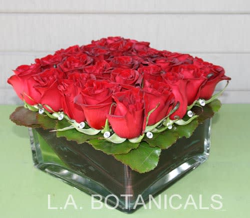 25 Red Roses in Low Glass Square - Show your devotion with something unique! 25 exquisite red roses are nestled together head to head in a low glass square vase lined with Ti leaves. &quot;Diamond&quot; gems peek between the roses for an added sparkle! 25 roses, approx. 10&quot; square.  NEED A TIMED DELIVERY? If you require an order to be delivered within a 3 hour window you MUST add our “Rush Delivery.” Specify your 3 hour window request in “Florist instructions” during the checkout process. (All deliveries are made between 9 a.m. and 4 p.m. only)