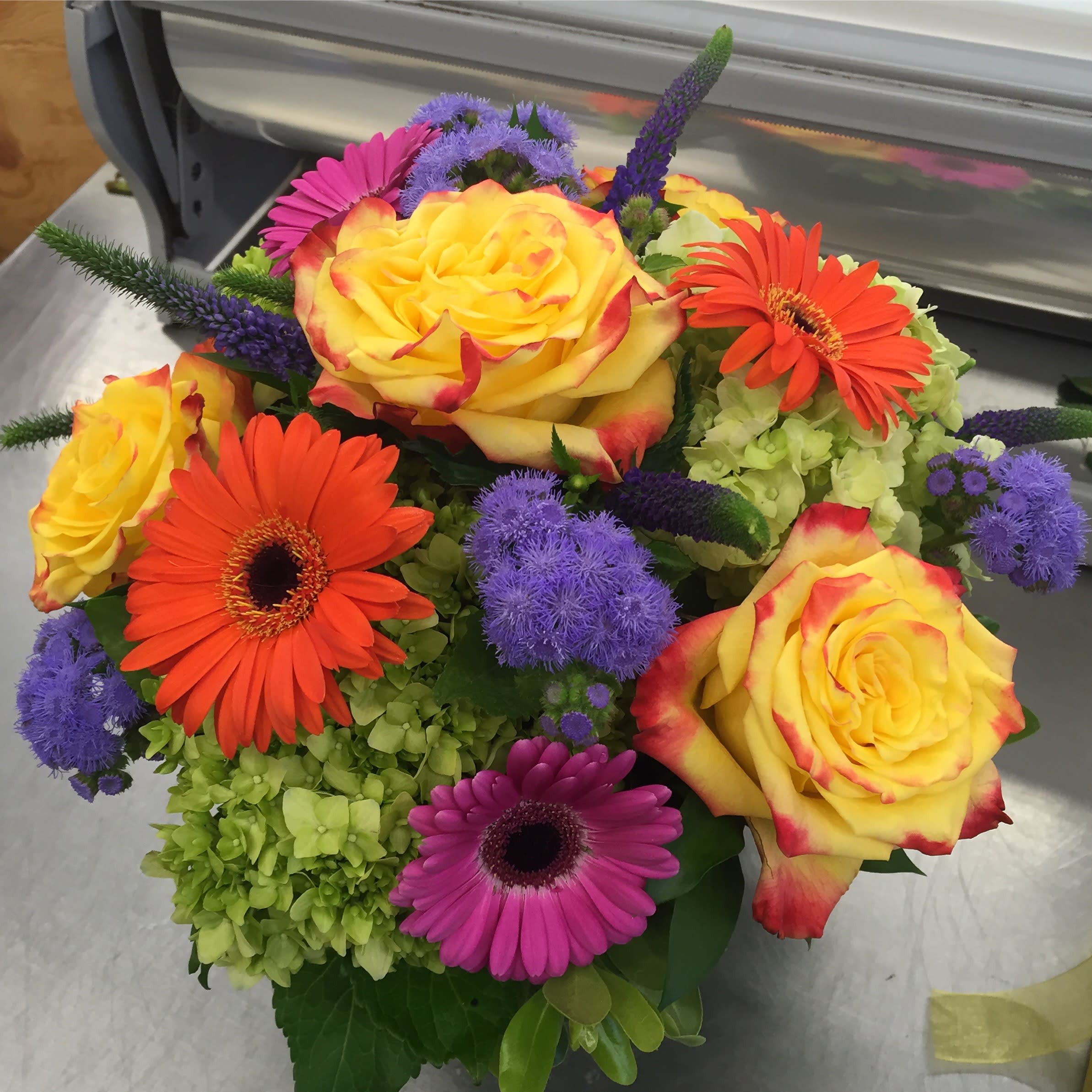 Full of Color Full of Color - This design is short and compact in a clear glass vase with a leaf wrap. Statice, roses, gerbera daisy's and hydrangea. Love the colors!