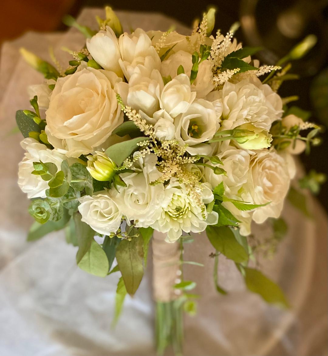 Rustic White Wedding Bouquet Rustic White Wedding Bouquet - This elegant design includes White Roses, Dahlias, Fressia, Lisianthus, and Astilbe, and is accented with various types of Eucalyptus. The handle is wrapped in burlap ribbon and pearl pins accent the handle. This bouquet measures approximately 10" in diameter and 12" long. All bouquets must be ordered at least 72 hours in advance.
