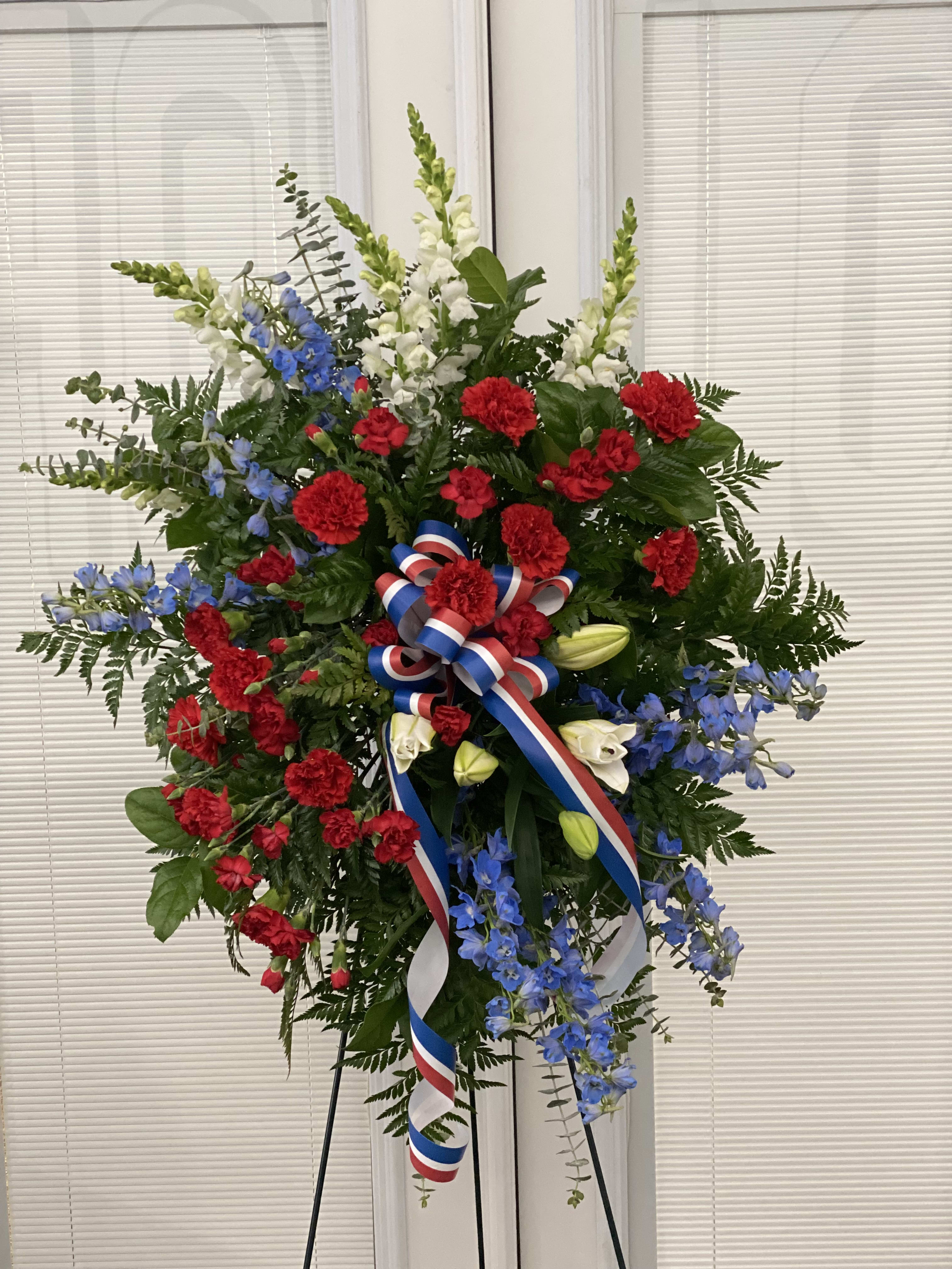 Sacred Duty Spray - Standing tall proud and patriotic this dazzling free-standing spray is like a fireworks display made of graceful flowers. Uniquely beautiful it's a lovely way to honor a great loss.