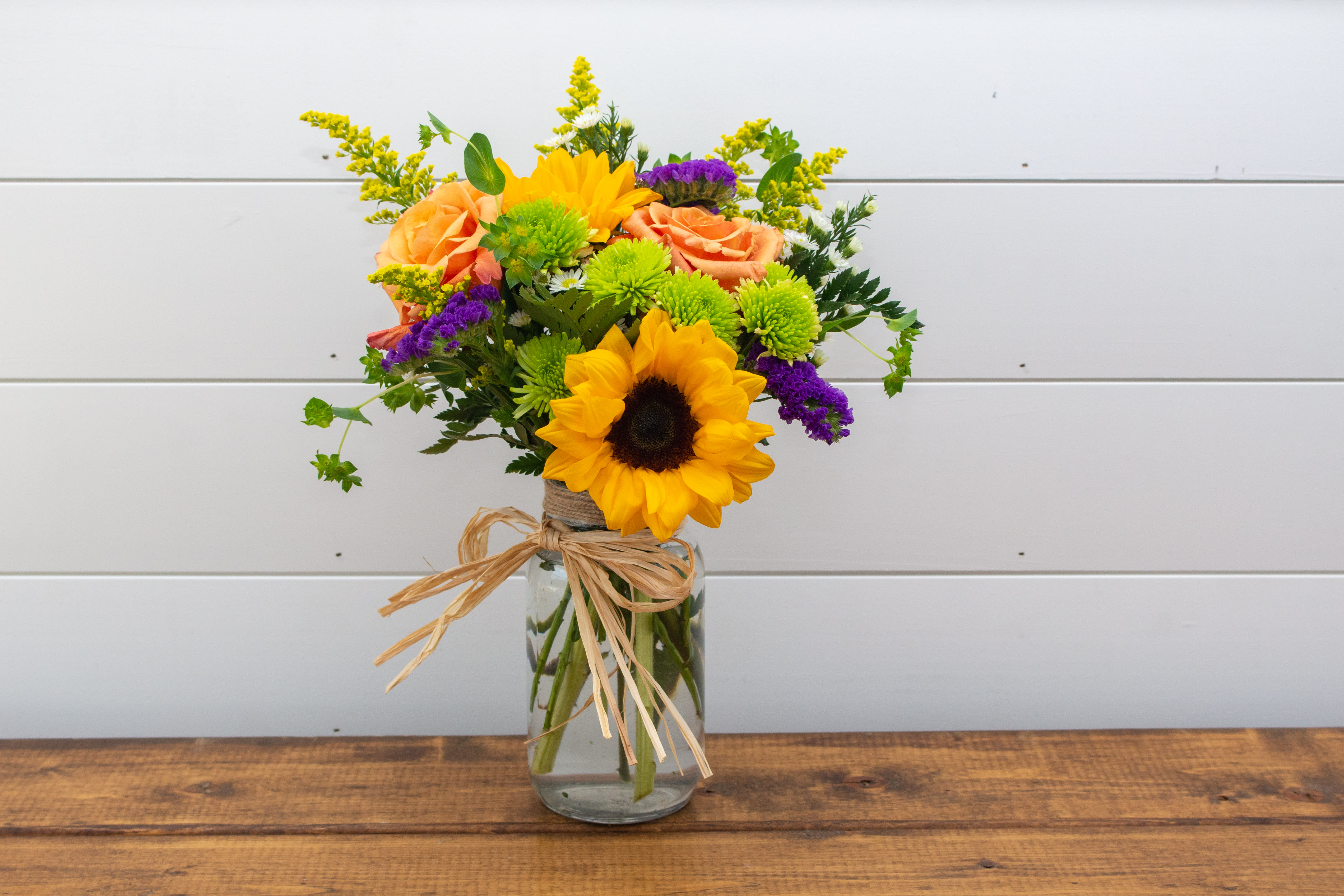 Your Momma's Mason Jar - Your Momma's Mason Jar is an original Forevermore Farm Floral arrangement. This arrangement is created with roses, sunflowers, purple statice, and fillers, finished with a rafia bow.