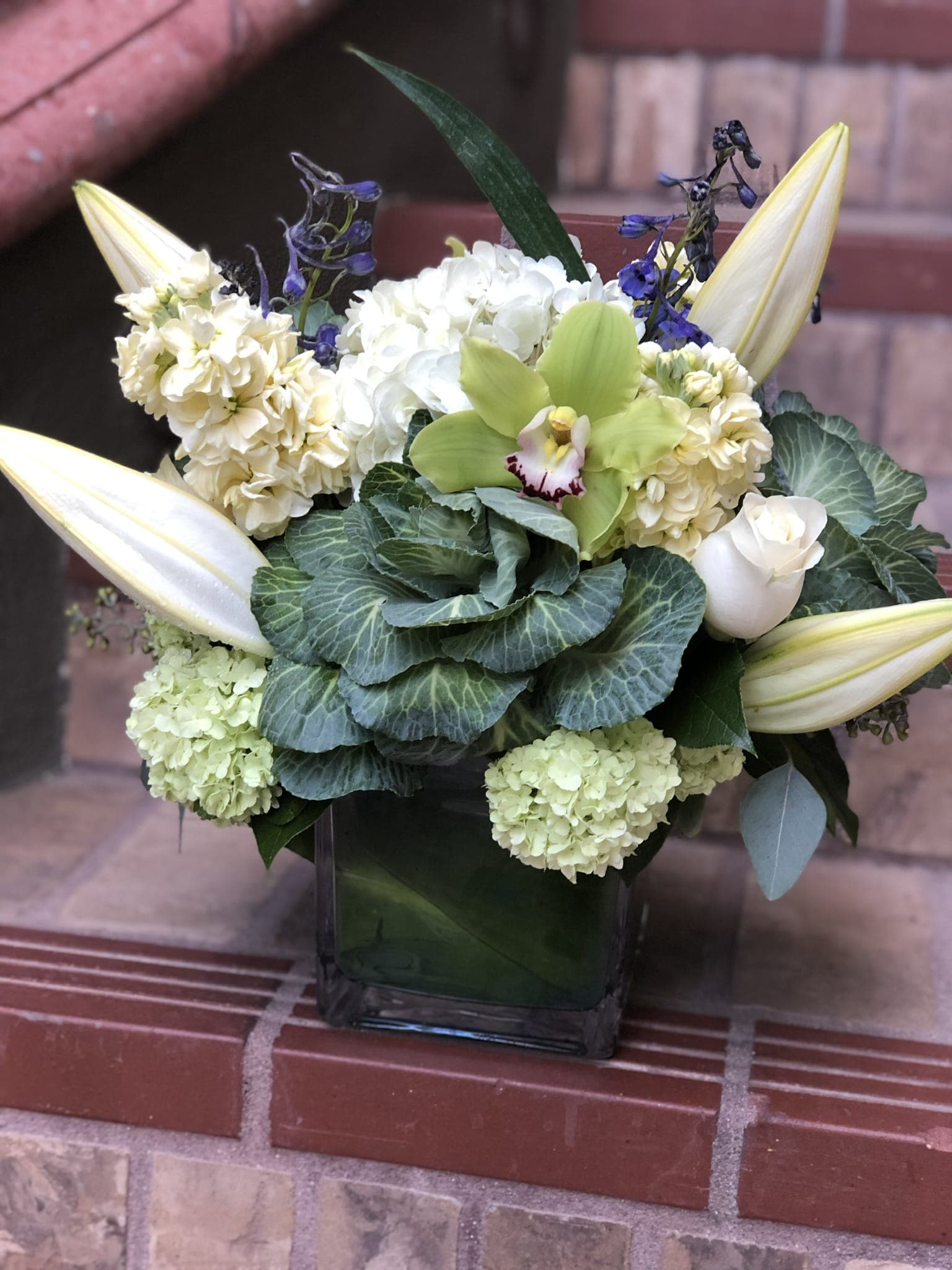 Farmers Garden  - Variety of fresh flowers from blue delphiniums, green orchids, lilies and flowery cabbage all arranged in a green glass. 