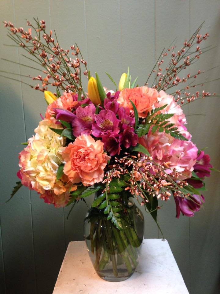 Pink n Peach Skies - This beautiful flower design has pink,orange and yellow hydrangeas,genestra, orange carnations, tulips and pink alstromeria in a clear vase. Vibrant colors will make Mom smile!