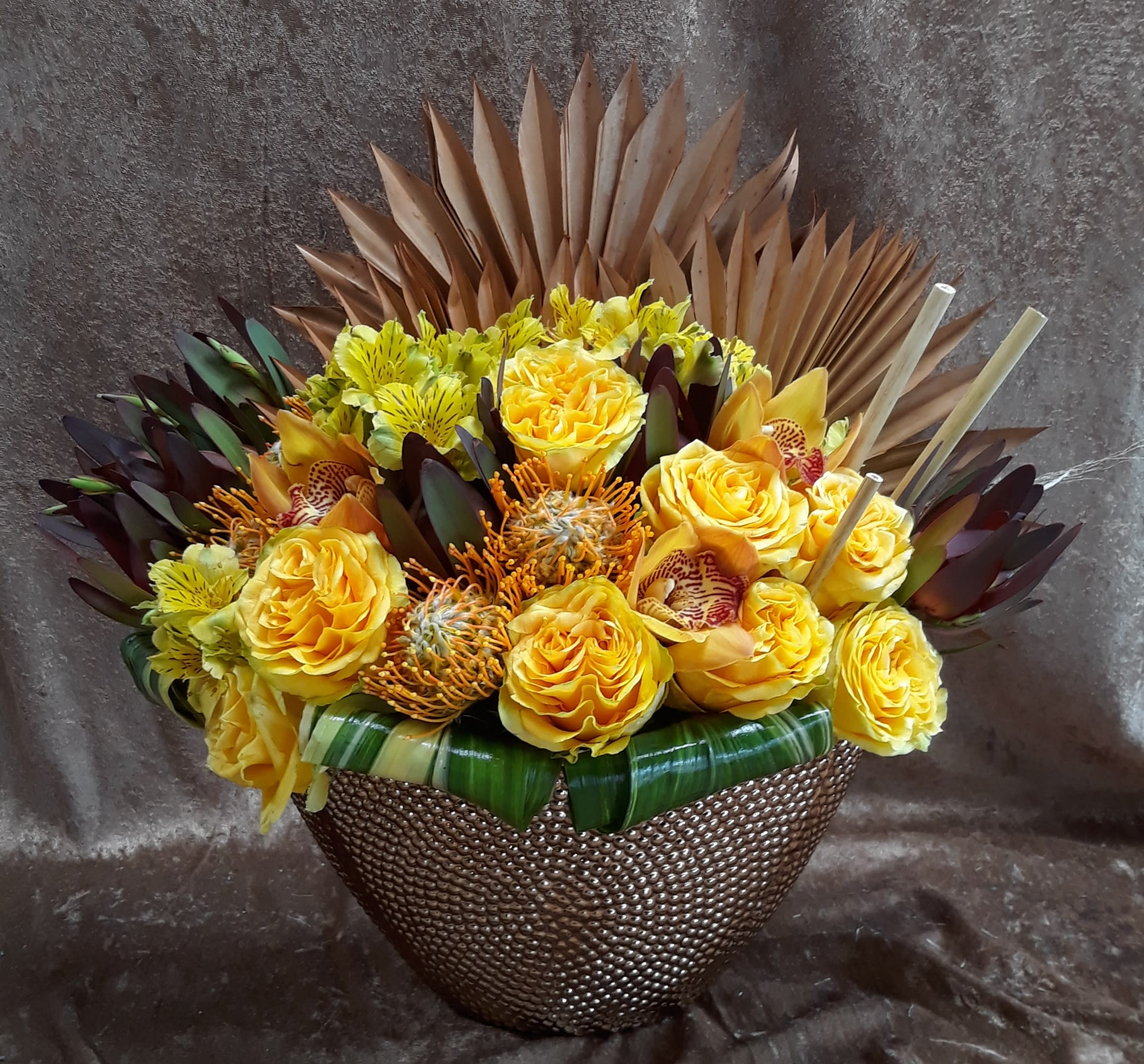 Regal Gold - Shown: DELUXE 19H 24W A nice mix of orchids, roses, pin cushions accented with dried elements for a unique and sophisted result 