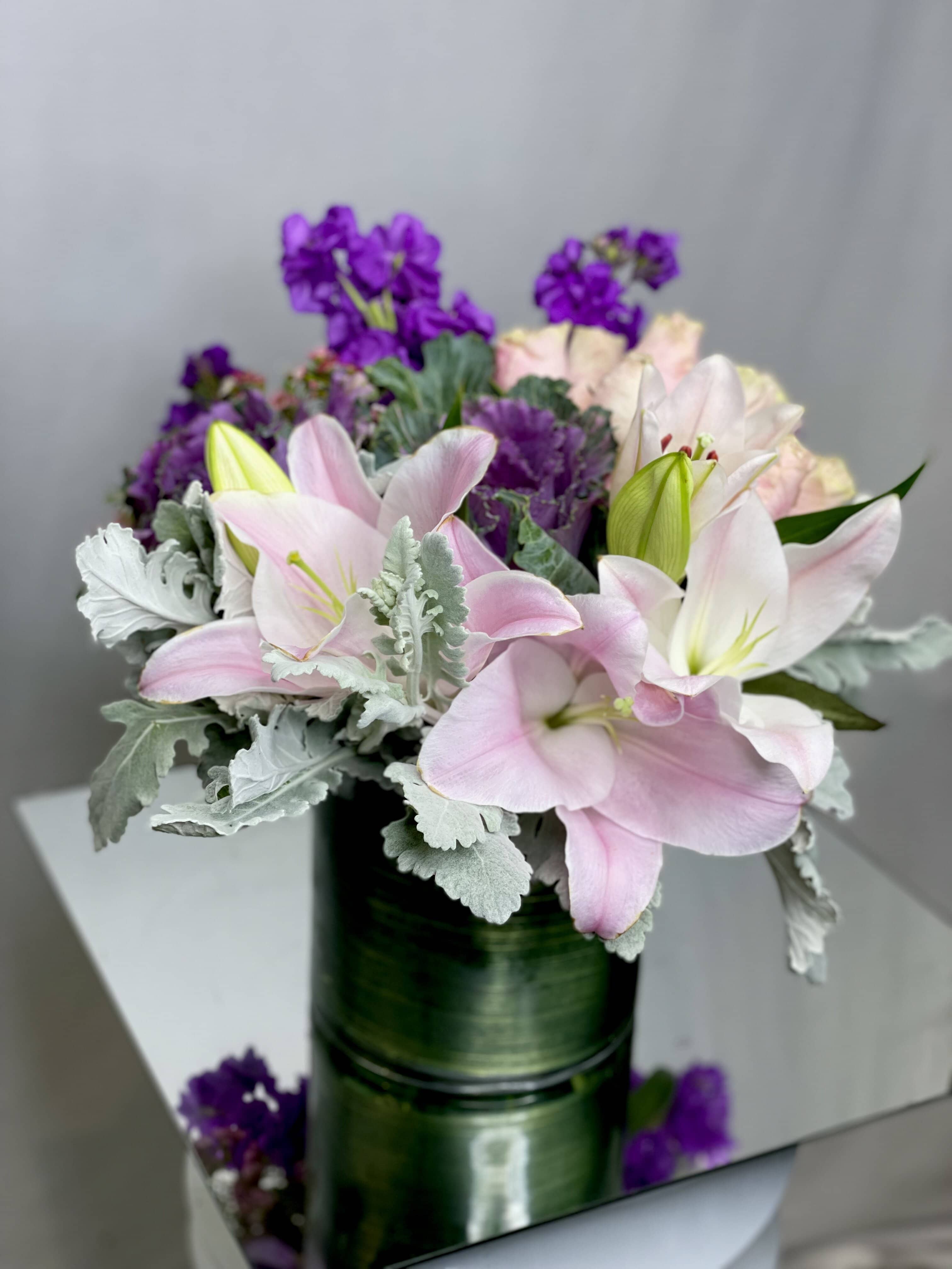 Pink & Purple Skies Pink & Purple Skies - A Beautiful arrangement featuring: Pink Lilies, Purple Stock, Light Pink Roses, Kale, and Dusty Miller arrange in a clear glass vase.