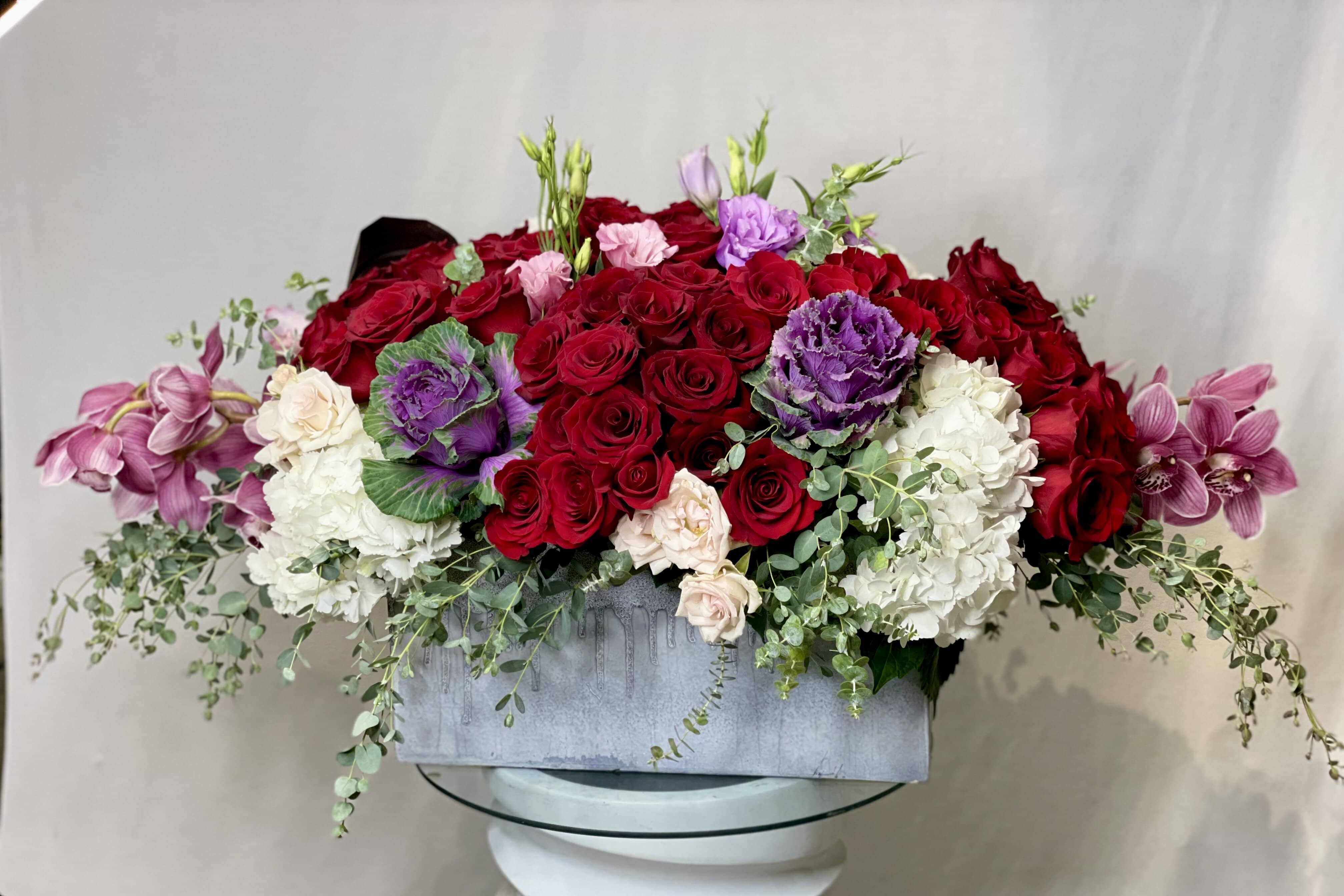 You Belong With Me - A Stunning Arrangement Featuring: Red Roses, Light Pink or White Roses, White Hydrangeas, Kale, Pink Cymbidium Orchids, Eucalyptus and added fillers arrange in a Large Ceramic Rectangle Vase.