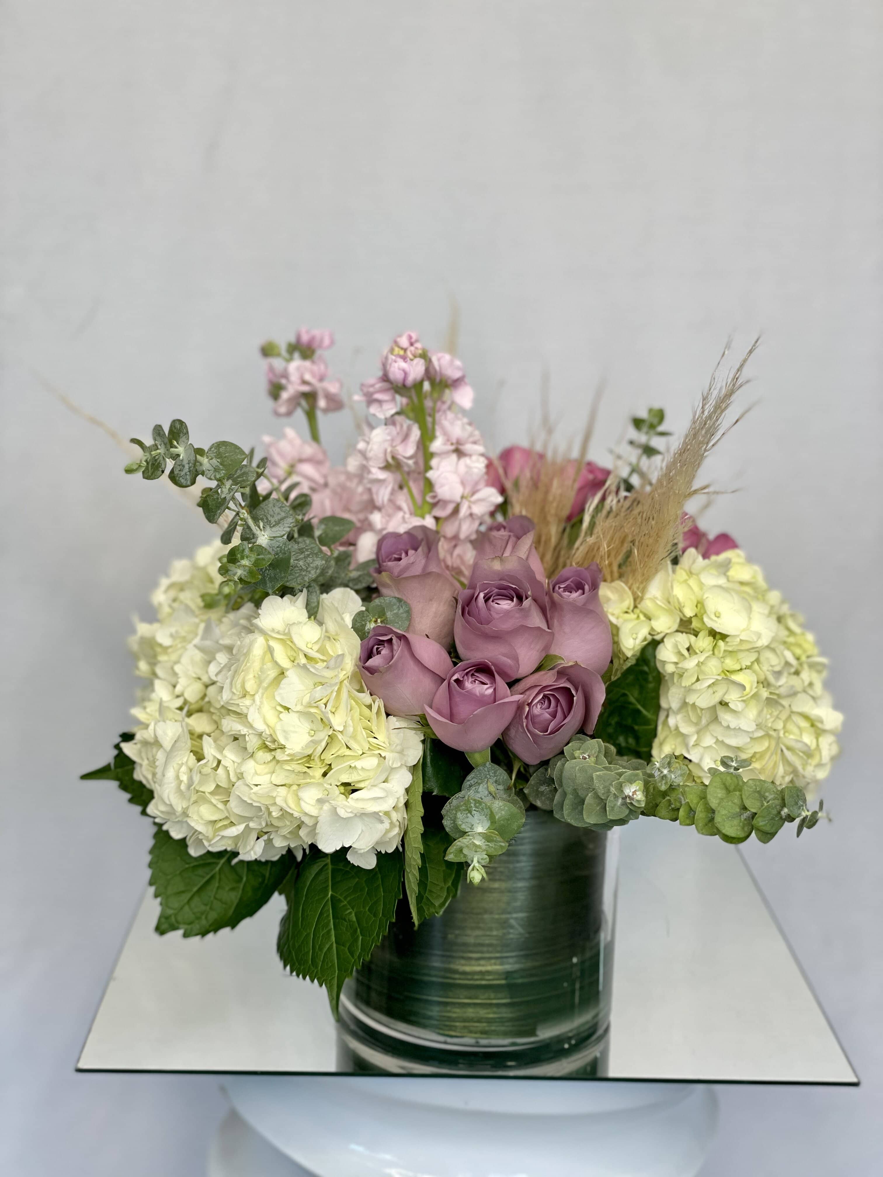 Bohemian Rhapsody  - A bohemian style featuring lavender roses, pink stock, white hydrangeas, eucalyptus, and assorted greens arranged in a clear glass vase.