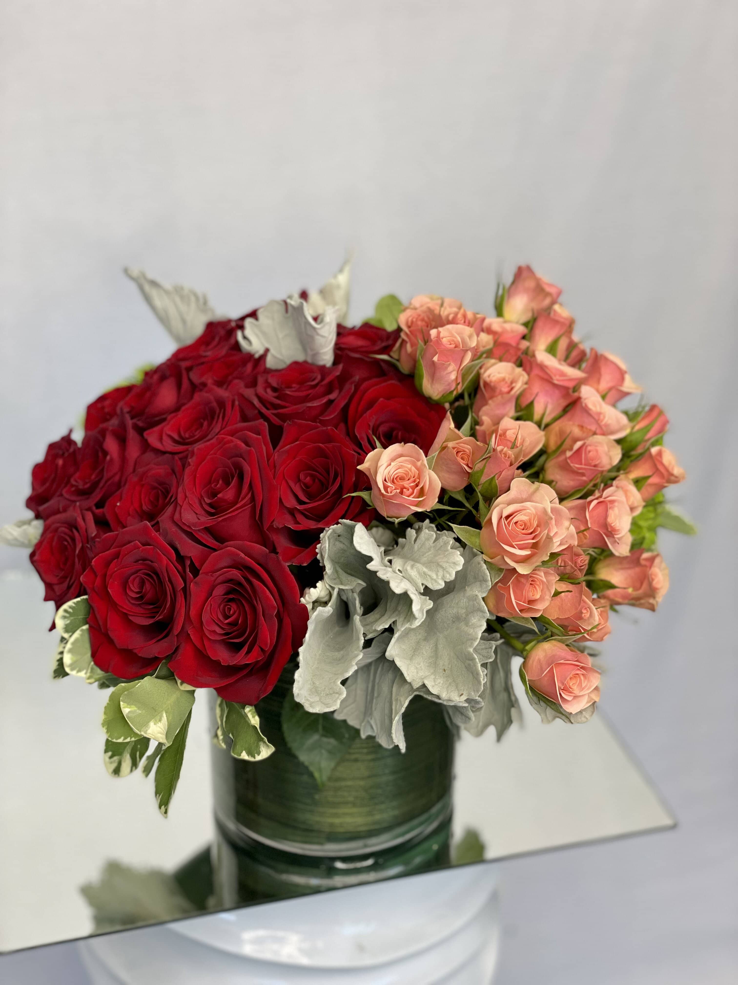 Flowing Beautifully  - An elegant arrangement featuring Red Roses, Orange Spray Roses, Dusty Miller, Green Hydrangeas and assorted green arranged in a clear glass vase. 