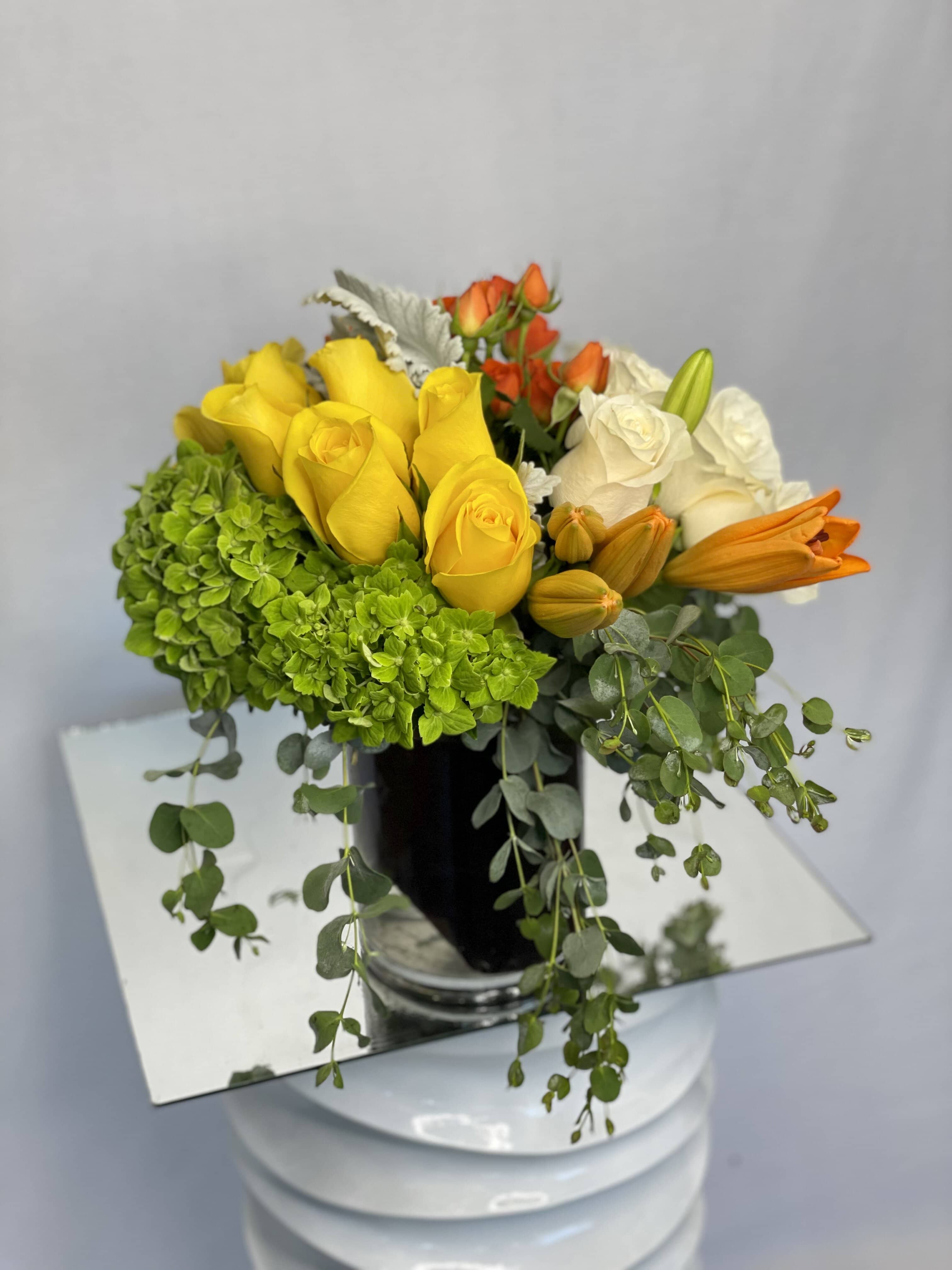 Creating Joy - Yellow Roses, Orange Lilies, Green Hydrangeas, White Roses, Eucalyptus, Dusty Miller are beautifully arranged in a clear glass vase.  