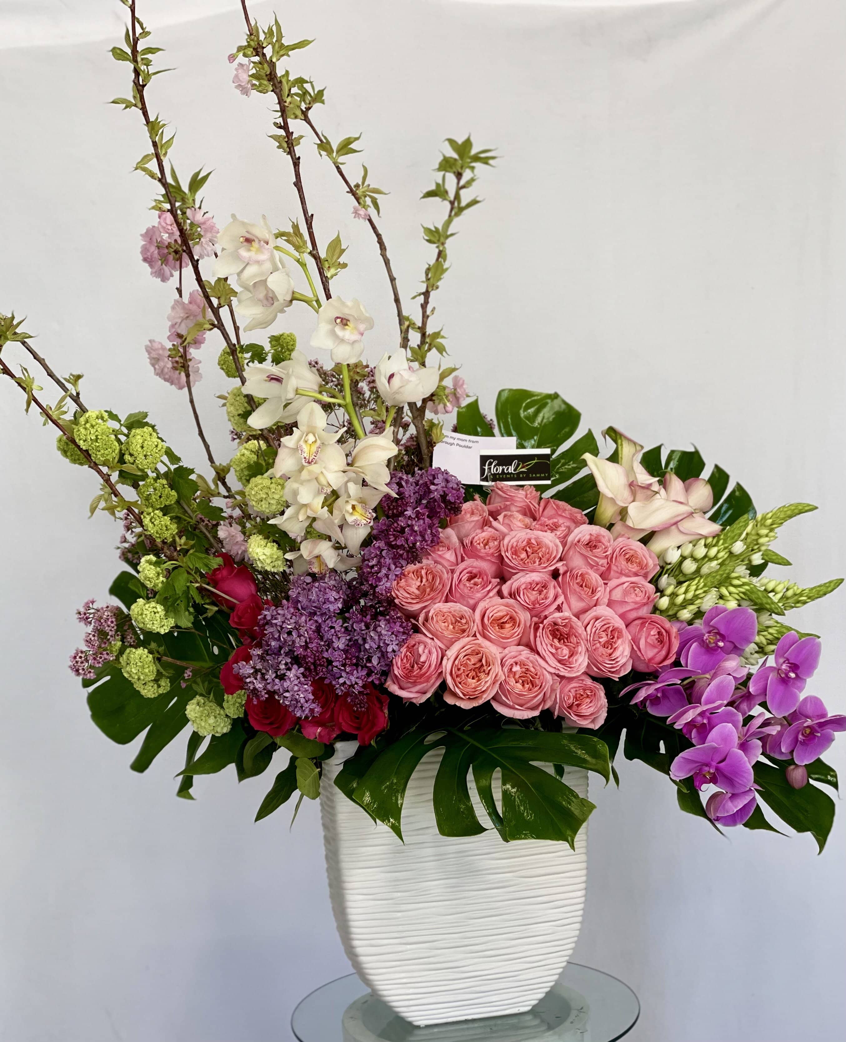 Wildest Dreams - Red Roses, Pink Roses, Calla Lilies, Monstera, Curly Willow, Purple Orchids, White Cymbidium Orchids. In a tall white vase.