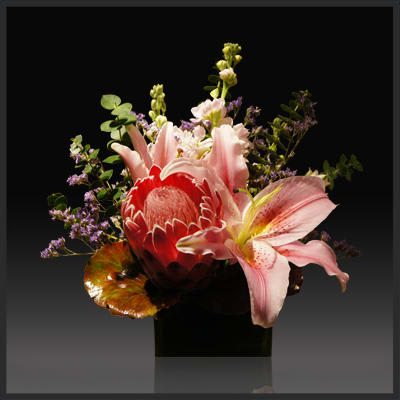 Queen on fire - Escape to tropical bliss with this stunning, sculptural presentation. banksia and fire fighter lilies, tropical red ti leaves and eye-catching red ginger are mixed with other colorful flowers and leaves in a decorative bamboo planter.