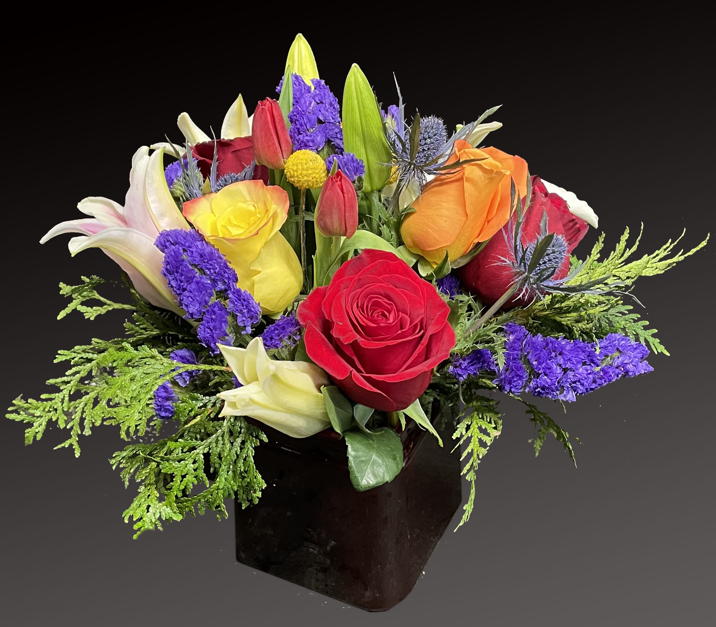 My Exquisite Beauty - This exquisite mix of feminine blooms is like a breath of fresh air! Yellow, orange and red roses are contrasted with a modern burst of blue. Blend them into a black ceramic container. 