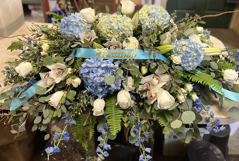 Comforting Thoughts - This double long, lavish casket spray has so many lush blooms. Lily's, orchids, hydrangea, roses, spray roses, delphinium, eucalyptus, curly willow.