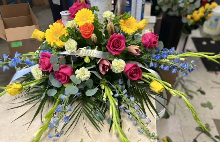 Our Hearts Go On - Casket spray with vibrant bright colors, gerbera daisy's, roses, delphinium, carnations, lily's, gladiolas and beautiful lush greenery.