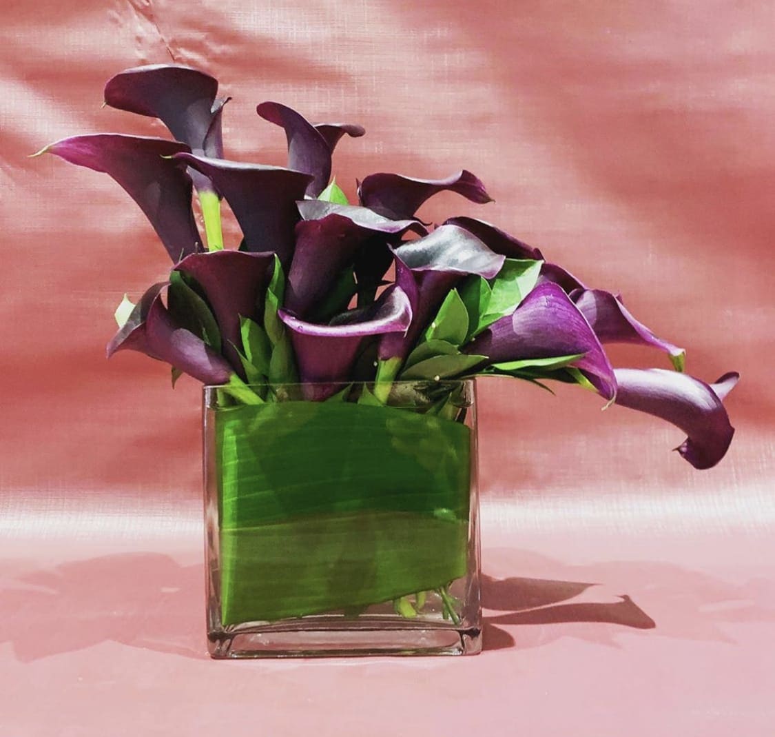 Custom Arrangement of dark purple calla lilies - Custom Arrangement of dark purple calla lilies &amp; greens in clear glass vase with leaf wrap.