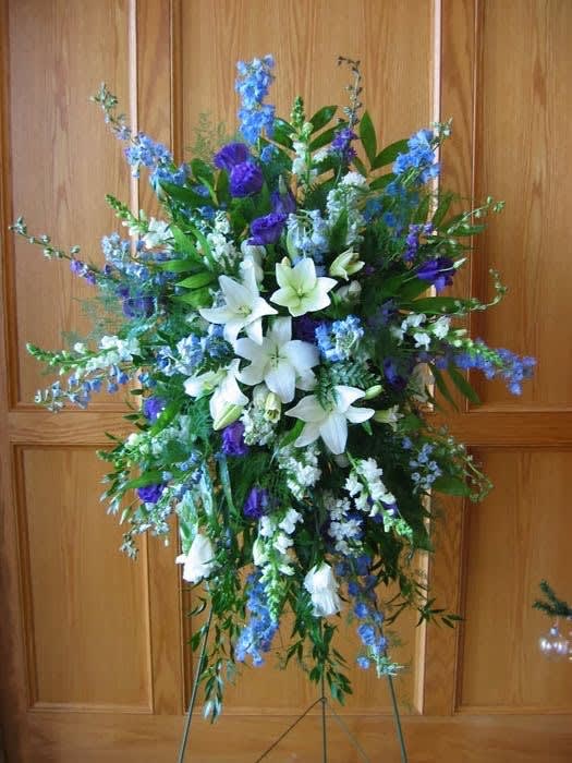 Heavenly Skies Standing Funeral Spray - Blue, white, and lavender and purple standing spray. Designed with white lilies, white or lavender roses, , white snapdragons, blue delphiniums, lavender and purple stock, and other assorted blooms in the appropriate color scheme.   Stands on a 60&quot; easel.