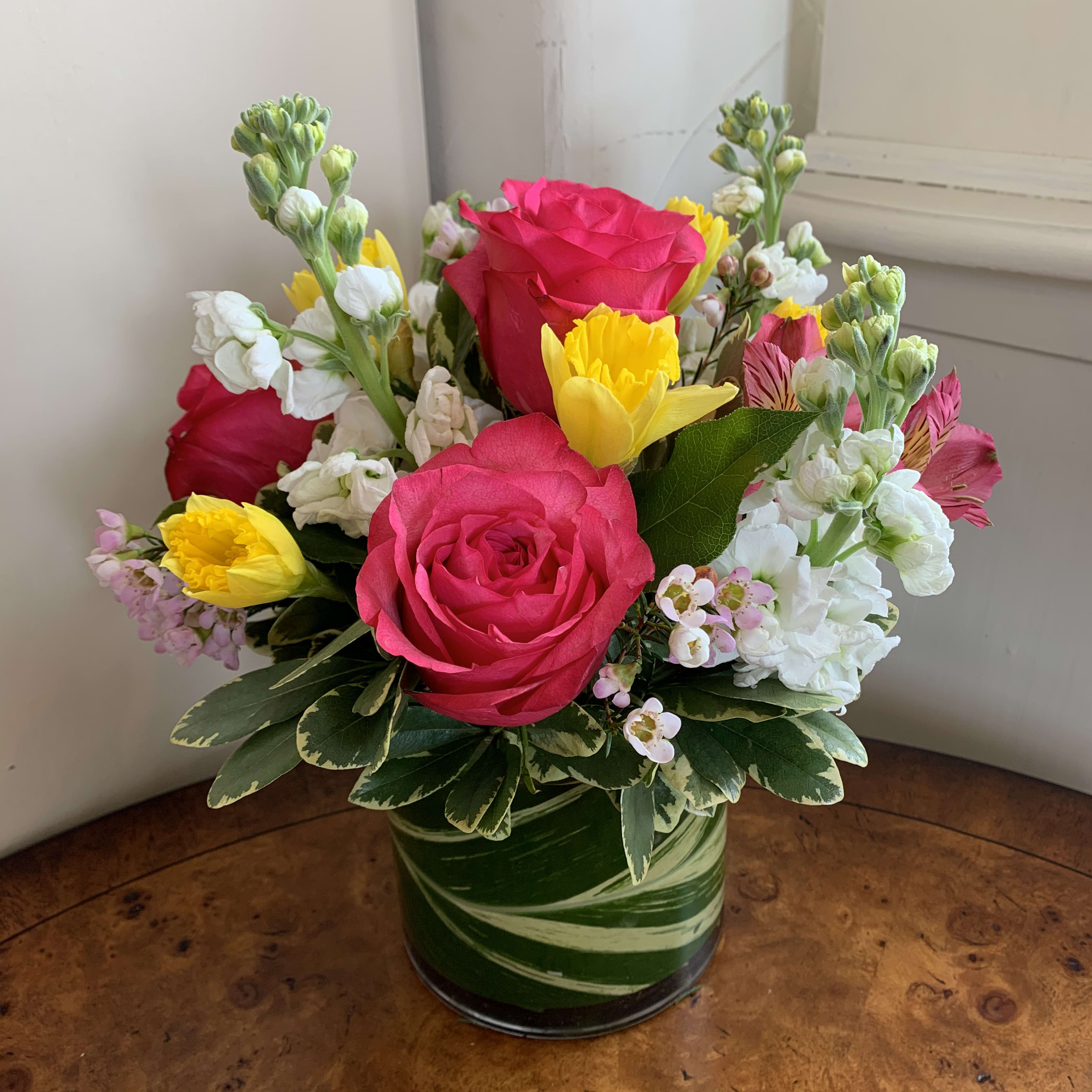 Smitten - Hot pink roses, daffodils, white stock, hot pink altromeria arranged with pink waxflower in a leaf lined medium gather vase. Approximatly 10&quot; tall by 10&quot; wide. 