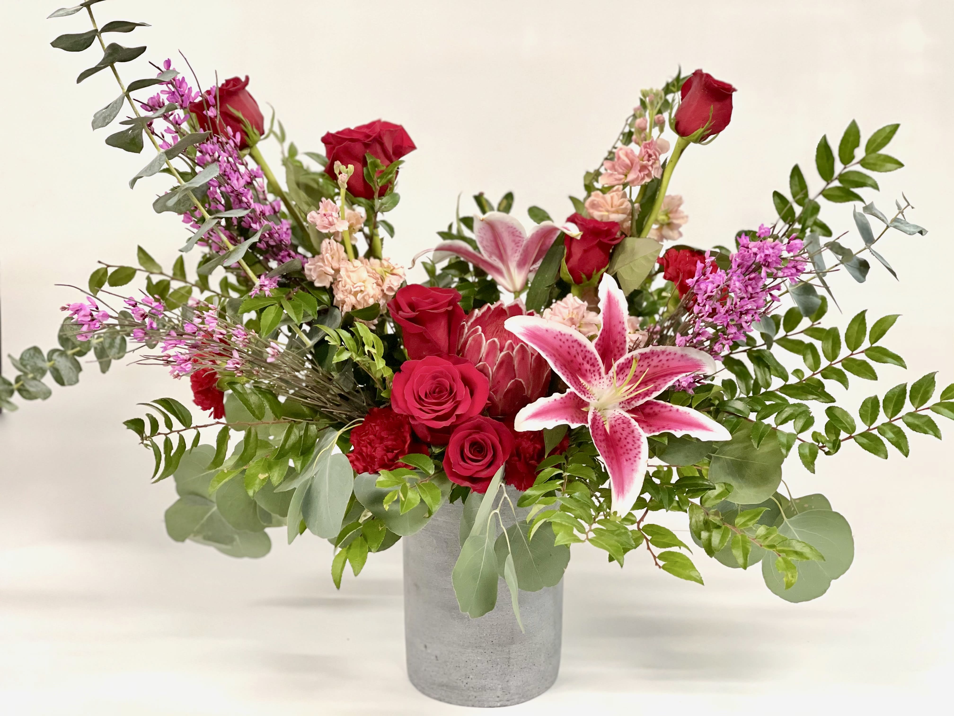 Sienna  - This over the top whimsical bouquet that is sure to wow! Filled ravishing red roses, stargazer lilies, eucalyptus and the ever popular tropical protea!