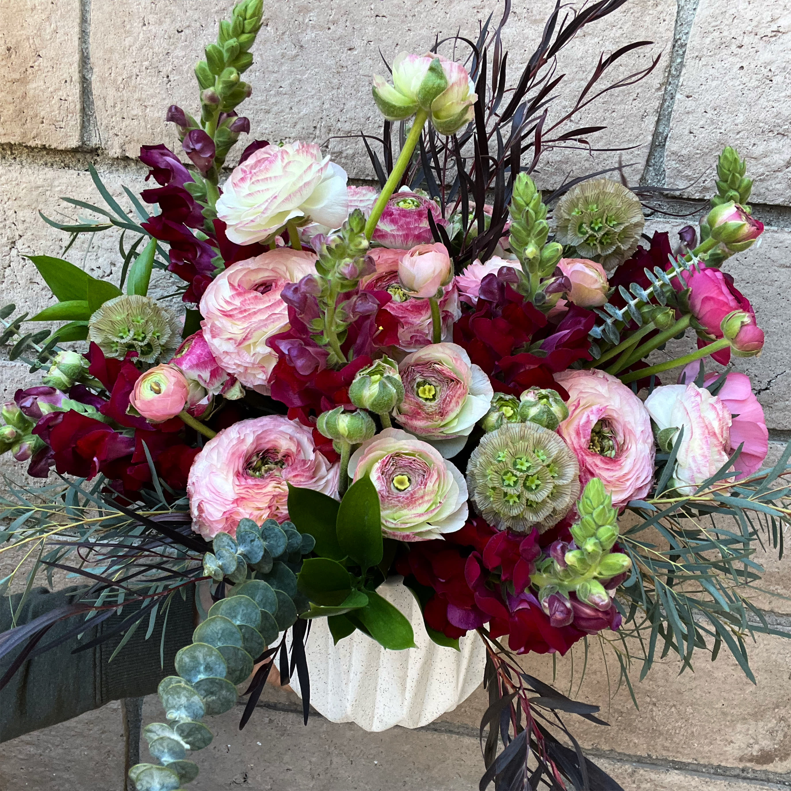 Head Over Heels - A dreamy mix of burgundy Snpadragons and mixed white and pink Ranunculus with accents of black feather Eucalyptus and Scabies pods. An exceptional arrangement for the romantic who had a little edge. 