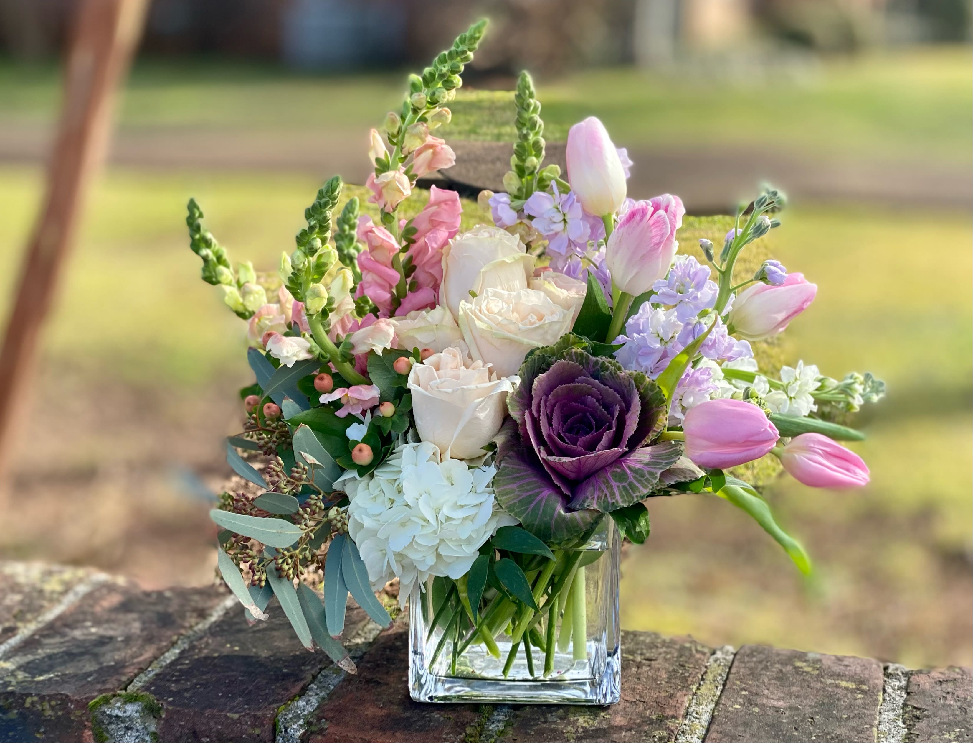 Adoring Devotion - Delight in an arrangement full of soft beauty and elegance. Cream roses are cradled by blushing pink flowers peach hypericum and ornamental greens. Cherish them always with a delicate expression of caring and joy.