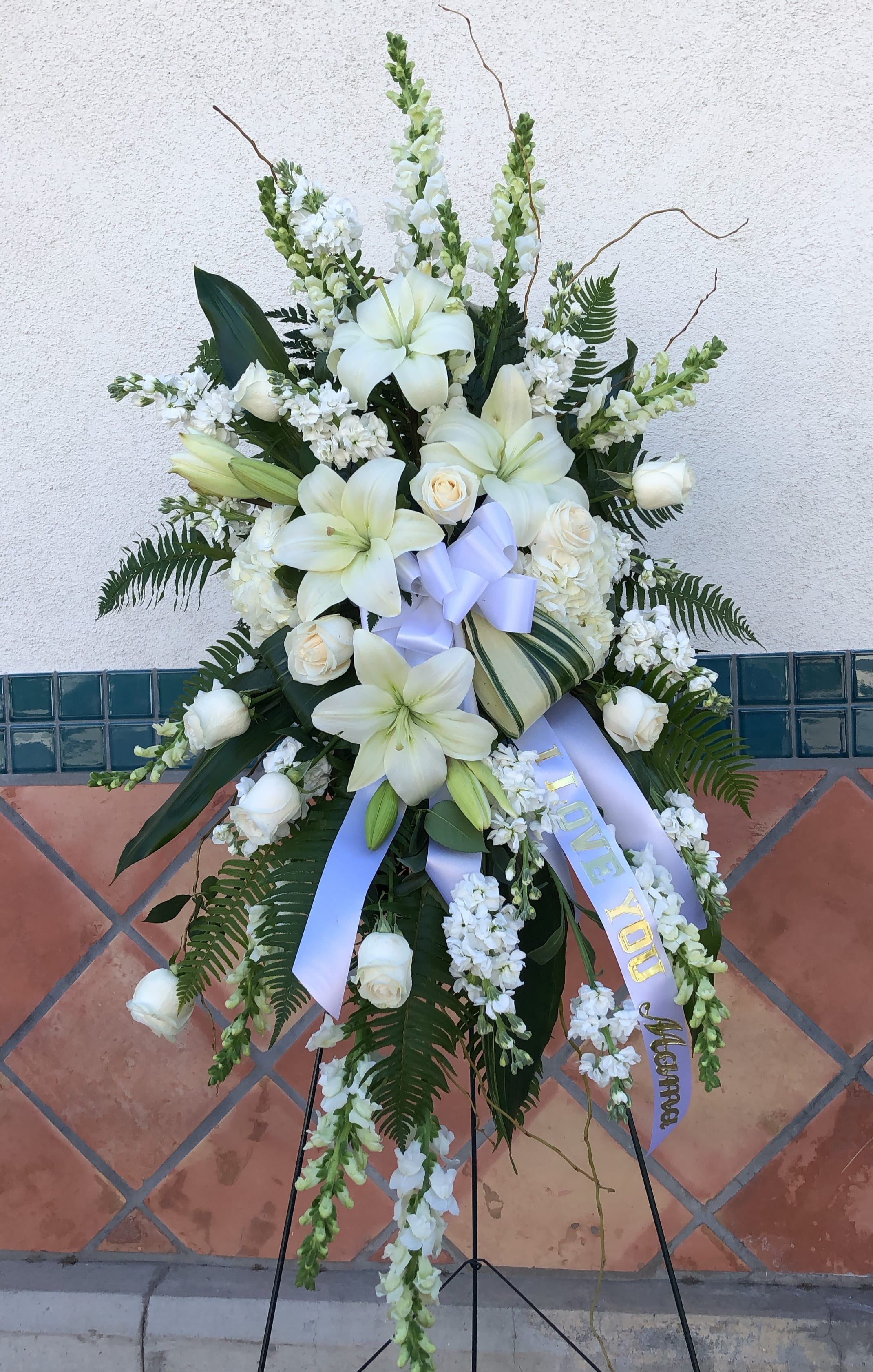Heartfelt Sympathy Spray - This beautiful spray includes white hydrangea white roses white oriental lilies white gladioli white stock pitta negra sword fern curly willow variegated aspidistra leaves and lemon leaf. Delivered on a wire easel.