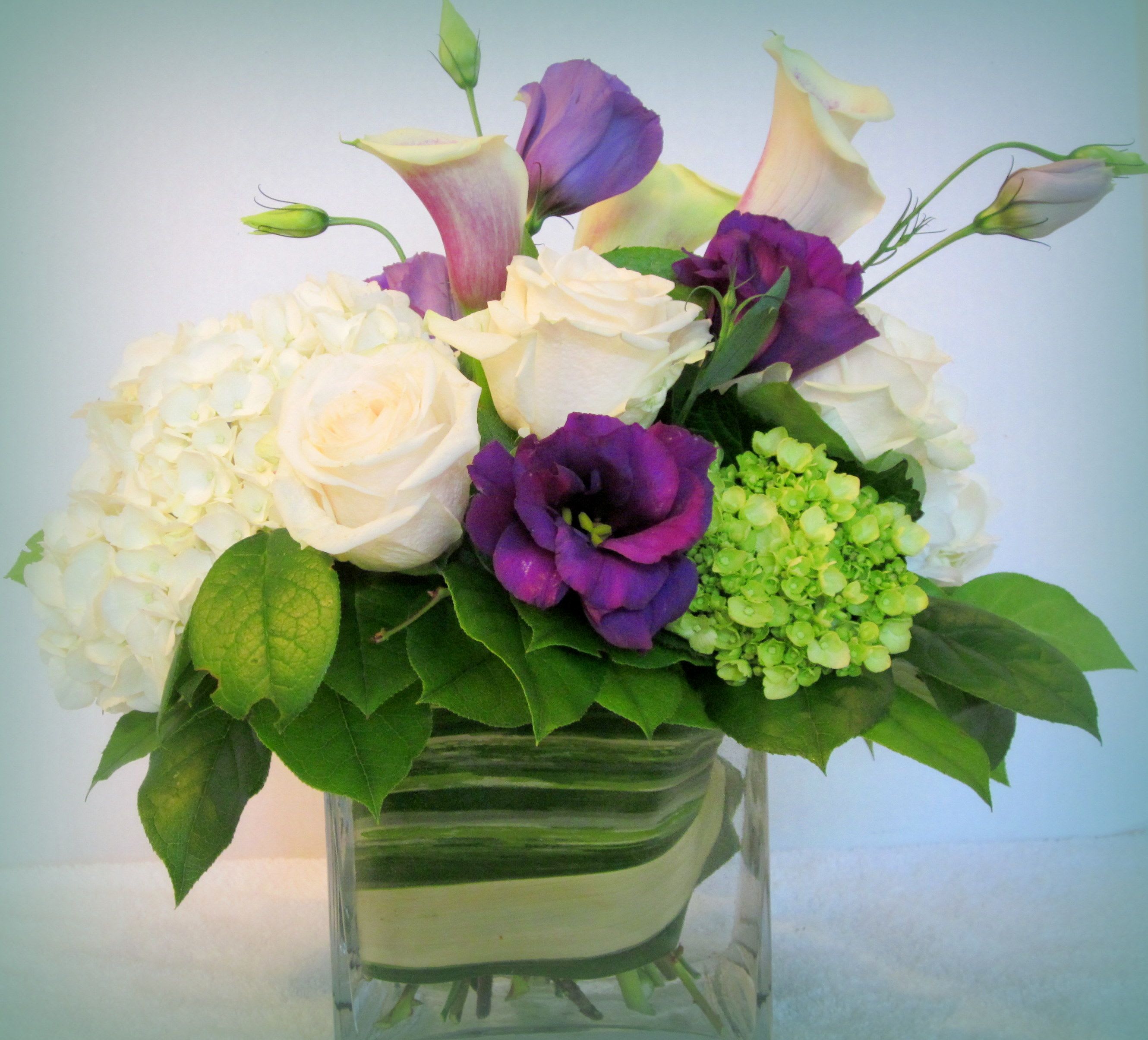 Green with envy - This plush floral arrives in a glass cube with calla lilies, lisianthus, hydrangea, and roses.  This elegant array of flowers will be a big hit.  