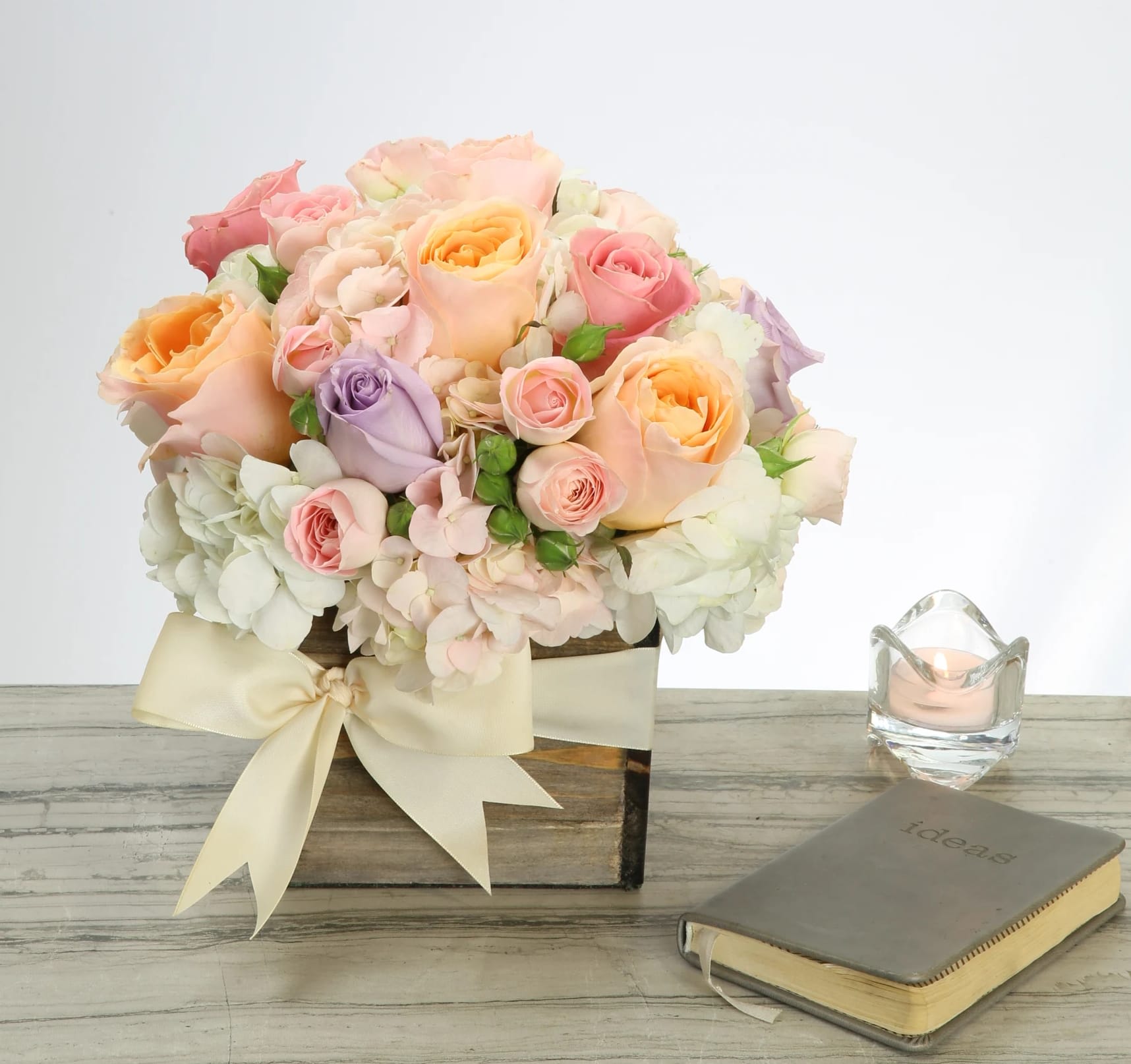 Pastel Perfection - Soft luscious pastel South American roses, embraced by Dutch Hydrangeas and a sprinkling of seasonal flowers make this delightful design one of calm and fragrant beauty. The custom bow tied around the box base puts the finishing touch on this lovely arrangement that will have everyone saying OMG!  Standard: Approx. 8&quot;  in a 6 X 6 Container Deluxe: Approx. 12&quot; in a 6 X 6 Container Premium: Approx. 16&quot; in a 8 X 8 Container
