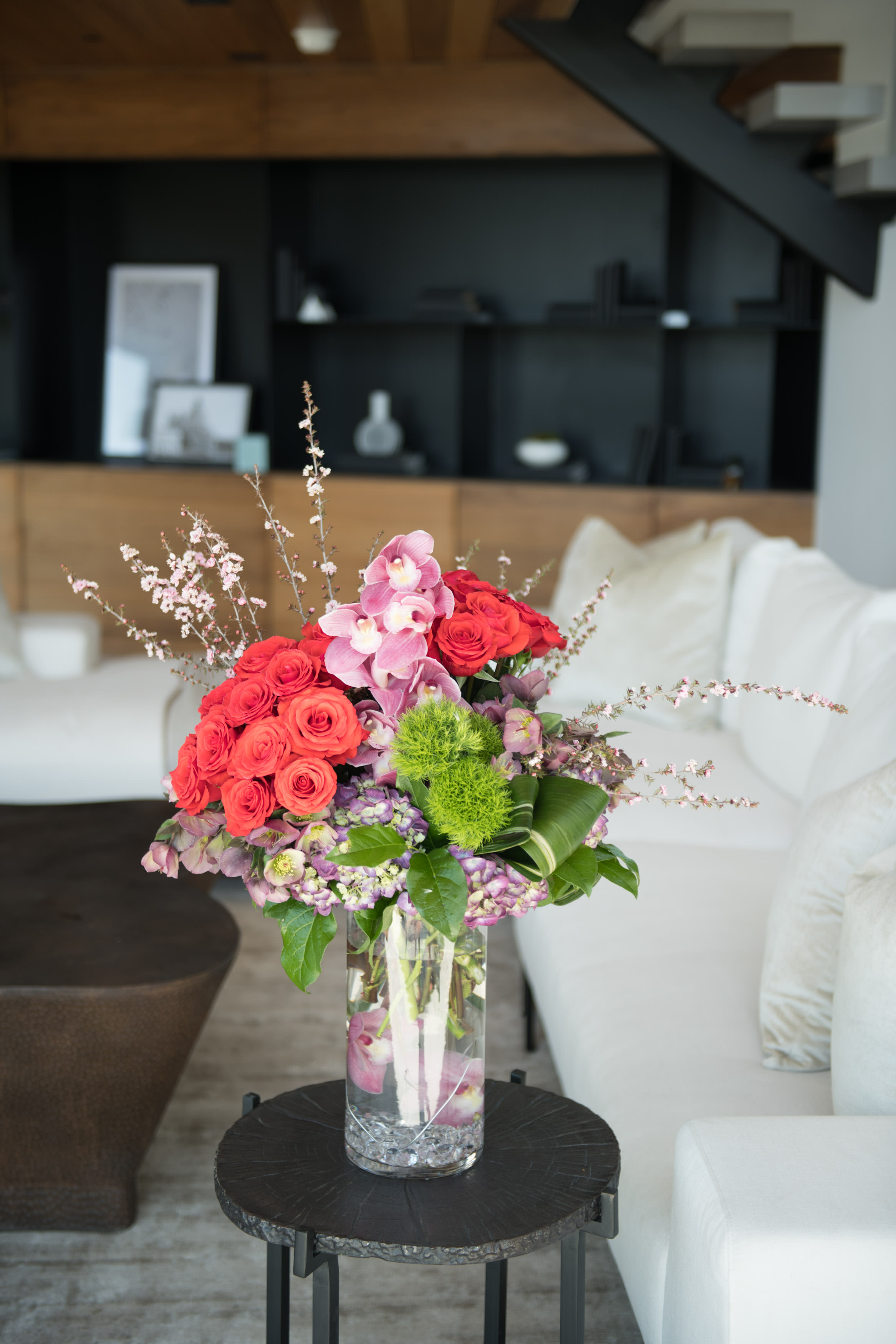 Grand Luxe Gala - Tall grand arrangement Bright Red roses, pink cymbidium, purple hydrangea, dianthus and other blooms. Designed in modern groupings in glass vase with sumerges orchids inside the vase. 