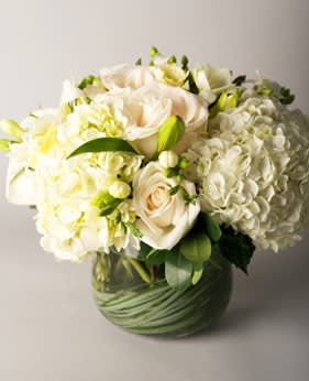 Le Blanc D'Origine Le Blanc D'Origine - A timeless lush and crisp all white arrangement featuring premium roses, hydrangea and complementary petals in a grass wrapped bowl.