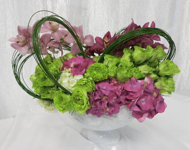 Swooping Sweetness - Pink Hydrangeas and Orchids accent swooping green Roses. Steel grass loops add to the extravagant movement. Vase dependent upon availability. 