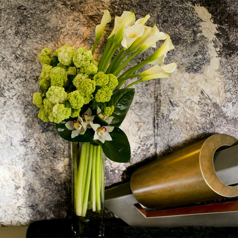 Green Goddess - White calla lilies, white cymbidium orchids and bright green viburnum adorned with anthurium leaves.  Floral subject to change based on seasonal availability. Containers subject to change based on availability.