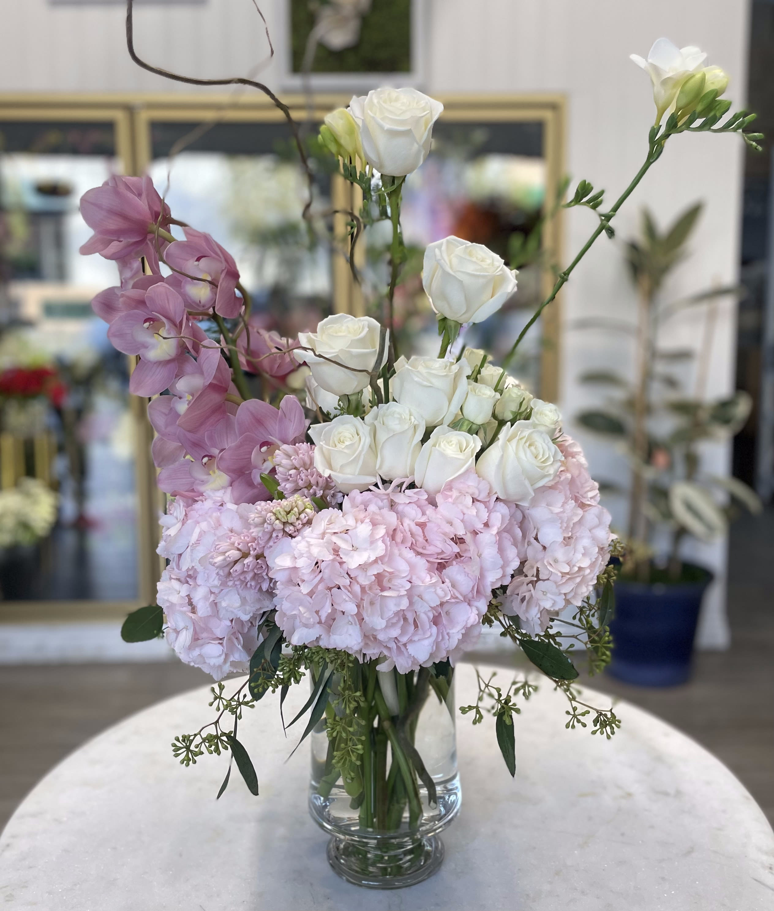 Pinks &amp; Whites  - Pink Cymbidium orchids, pink hydrangeas, white roses, spray roses, and assorted greens in a clear glass vase. 