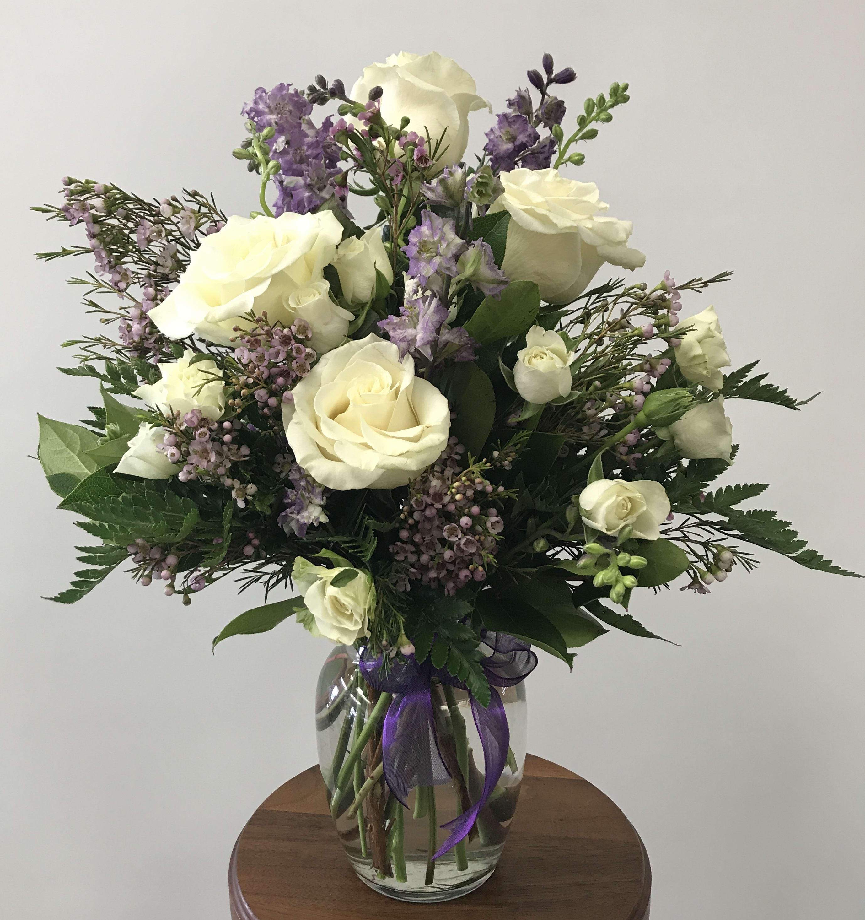 Enchanted Cottage - As enchanting arrangement of whites and lavenders with flowers such as white roses and purple larkspur mixed with delicate lavender accents for an elegant English garden look. The decorative bouquet is finished with a pretty satin ribbon.  Flowers may vary due to availability.  Orientation: one-sided