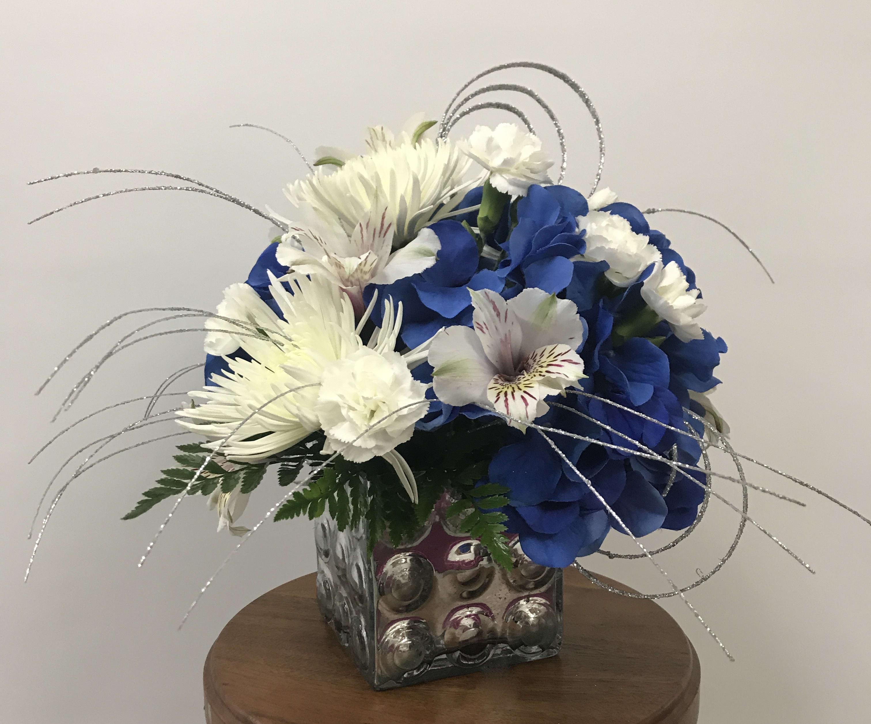 EIU Forever - Designed in EIU colors, this cube arrangement makes the perfect gift for students AND faculty! Blue permanent hydrangea, white spider mums, daisies, and miniature carnations with silver accents. 