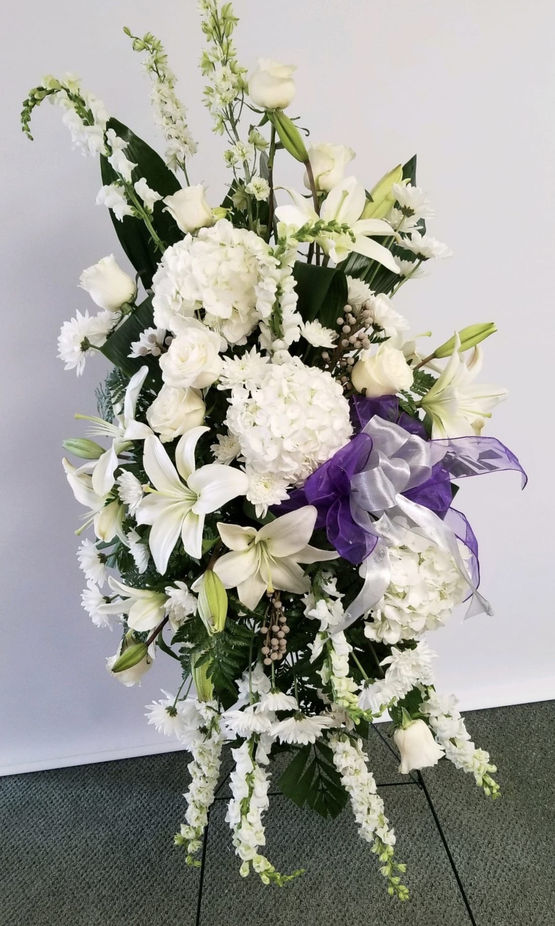  Magnificent Life Spray - A magnificent symbol of love and peace, this pure white and green spray conveys your sympathy with elegance and grace. Ribbon only on request.  This gorgeous array of white roses, white lilies , white hydrangea, white snapdragons, white larkspur, white cushion spray chrysanthemums and berries is accented with green ti leaves and other greenery.      Orientation: One-Sided