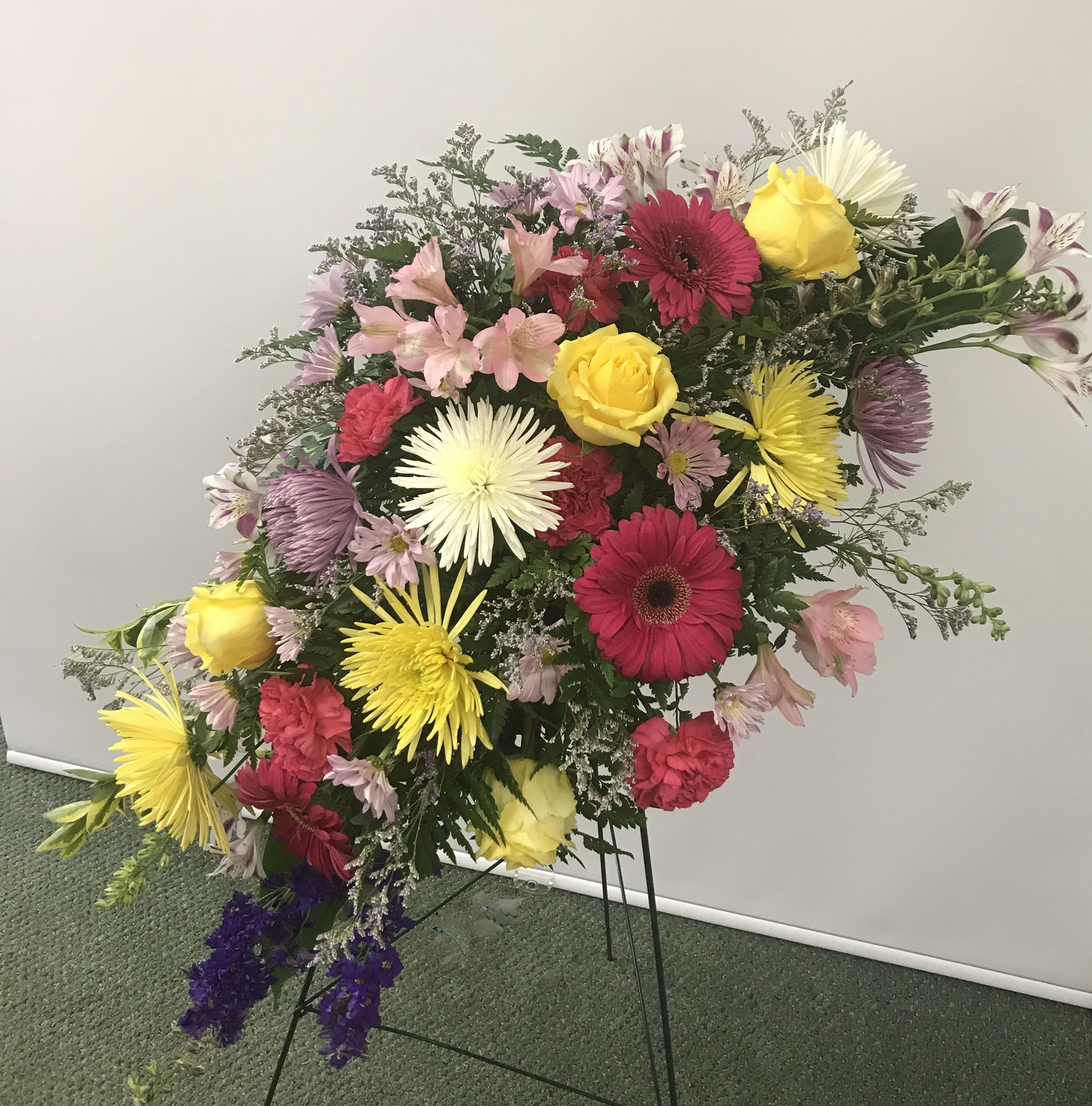 Heavenly Grace Spray Heavenly Grace Spray - A sublime garden of rich yet subtle hues is a touching tribute to a lifetime of memories and special moments as varied and dear as this palette of blooms. A lovely assortment of flowers such as roses, Larkspur, spider mums, gerberas, carnations, daisies and statice, on a classic easel. Orientation: One-sided