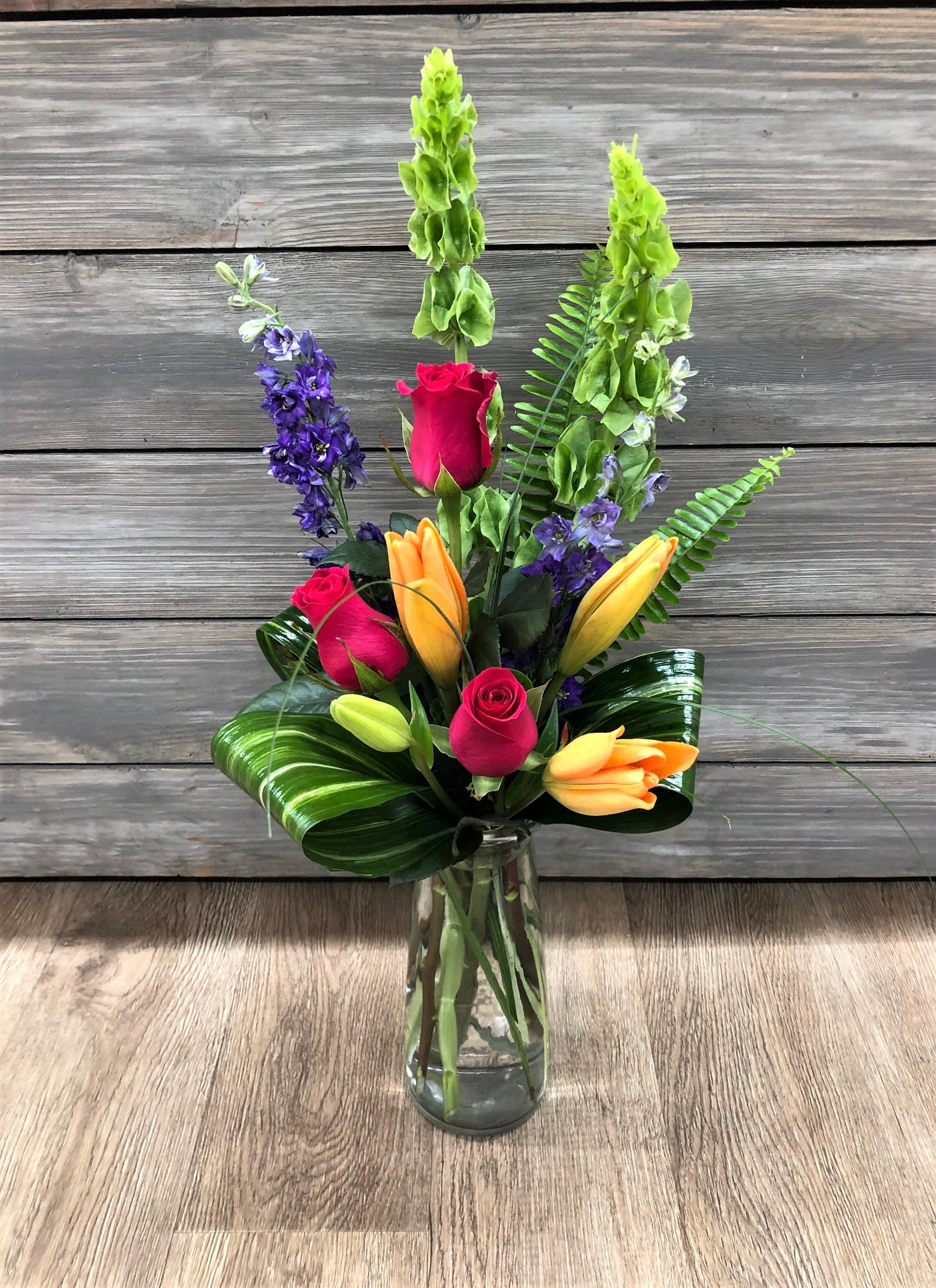 Brilliant Elegance Bouquet Brilliant Elegance Bouquet - Simple and elegant , yet bright and bold. Lilies, roses, larkspurg and bells surrounded by aspidistra, fern and lily grass greenery Vase may be substituted.
