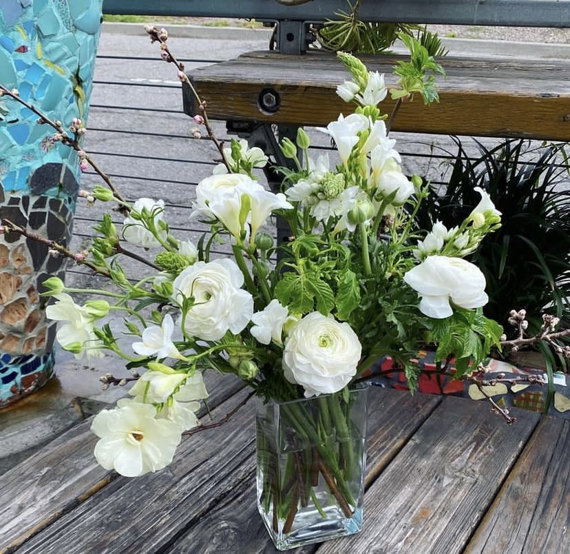 With Sympathy With Sympathy - A sympathy arrangement with Star of Bethlehem, freesia, ranunculus, Persian buttercups and Spring blossoms. Clear glass vase included.