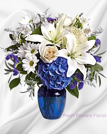beauty in Blue beauty in Blue - Blooms such as blue hydrangea, crème roses, graceful white oriental lilies, white alstroemeria, a white disbud mum, purple statice and lavender limonium are accented by seeded eucalyptus and salal in a stunning cobalt blue glass vase. Orientation: One-Sided