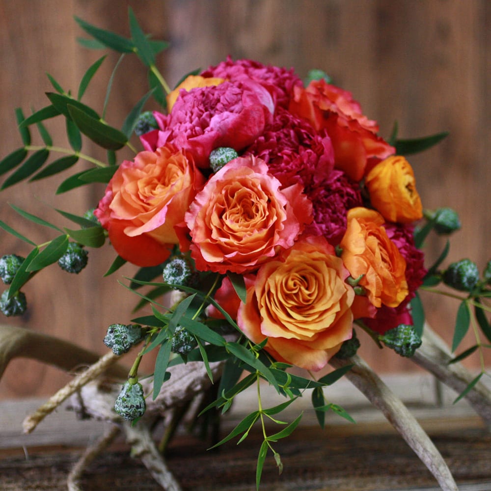 Designers Choice: Wild West - An arrangement of free spirit roses, fuchsia accent flowers and trailing greens in a clear glass vase. Antlers or fantail willow branches will be used depending on availability.