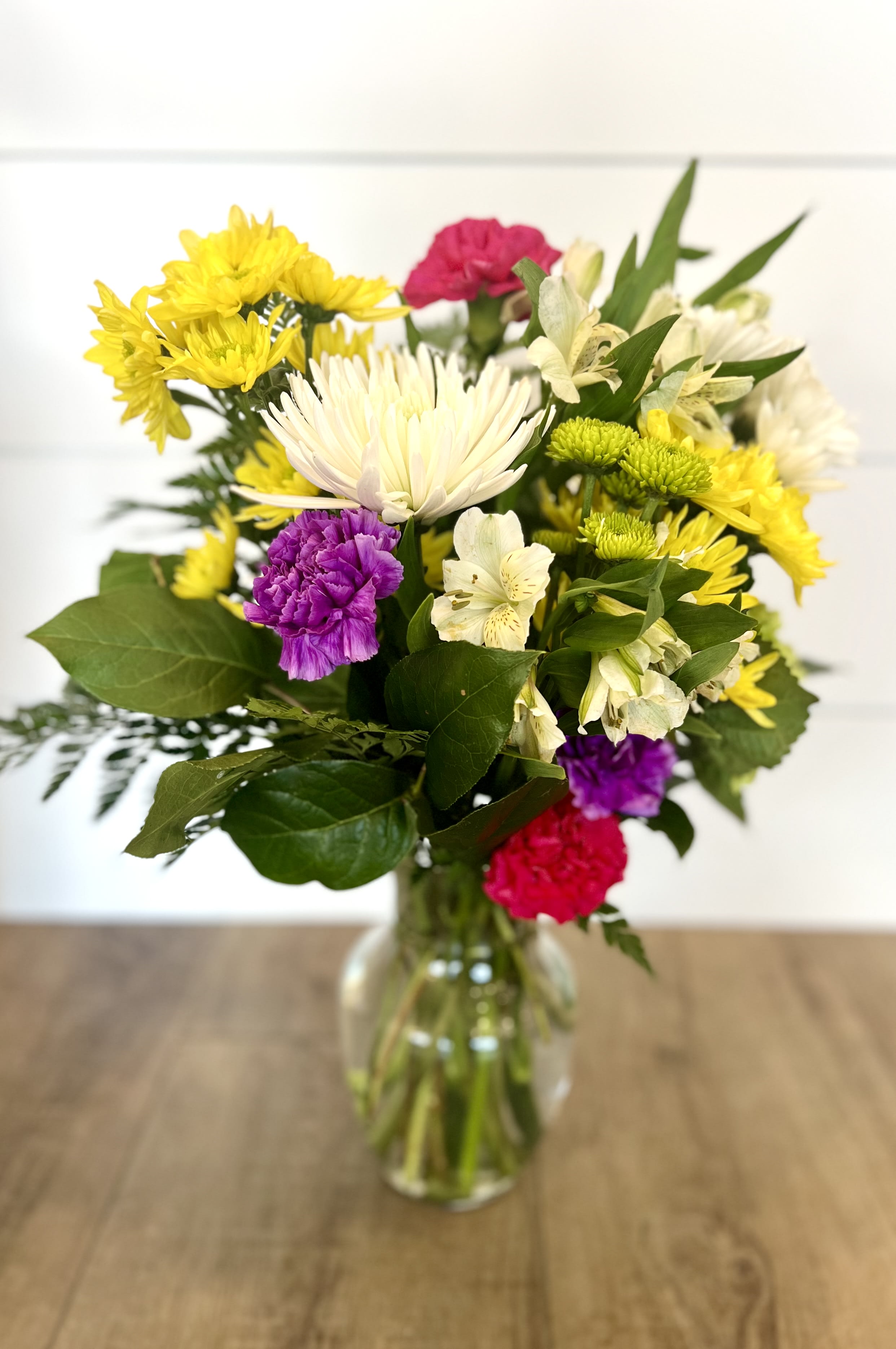 Pocket Full of Sunshine Pocket Full of Sunshine - A Bright arrangement featuring: Daisies, Poms, White Alstroemeria, Green button poms, Pink and Purple Carnations, and a green hydrangea.