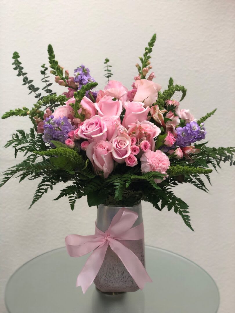FLOR PALIDA (PALE FLOWER) .2 FLOR PALIDA (PALE FLOWER) .2 - "lovely lady with this feminine bouquet of pastel and pink flowers. The pretty pink arrangement is a heartfelt choice. Name after someone’s favorite love song • A feminine mix of pink roses, pink spray roses, pink snap dragons and light purple stocks, green filler on season, pink Alstromeiras. Garnished with leather fern are presented in a charming pink stone vase. • SET: All-Around"