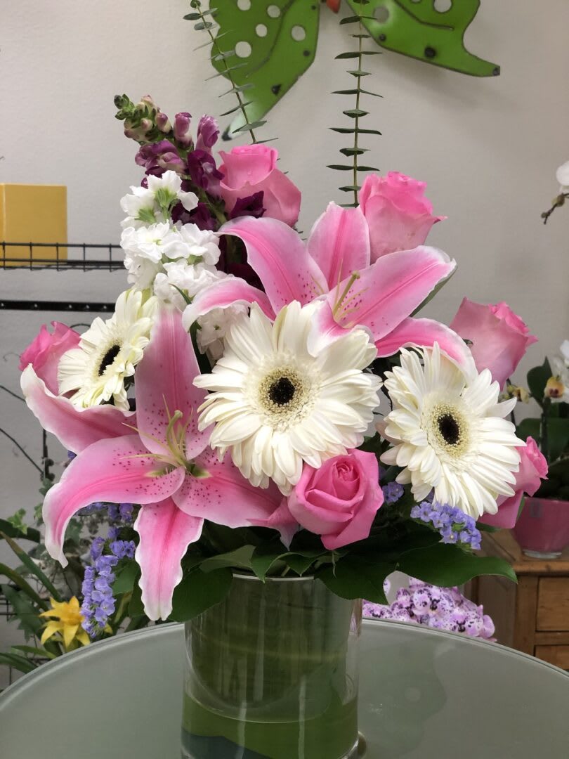 PLAYFUL PINK - &quot;Bright white daisies dance with happy pink lilies and fabulous fuchsia stock in this playful bouquet! Wrapped with a Ti leaf in a modern cylinder vase, it’s a joyful gift for any occasion.  Pink Asiatic lilies, fuchsia stock, white daisy spray chrysanthemums, and raspberry sinuata statice are accented with sword fern, variegated ti leaf, and lemon leaf. Delivered in a Clear Glass Cylinder vase.  SET: All-Around All prices in USD ($)&quot;