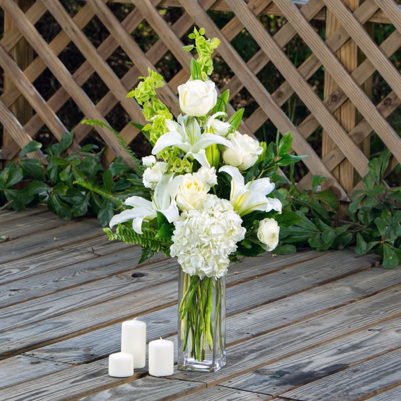 Tranquility  - All white arrangement with white oriental lilies, hydrangeas, roses, ranunculus and bells of Ireland. Complete with 10&quot; clear cylinder vase. Suitable as sympathy bouquet. 