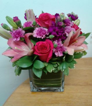 Pampered in Pink Pampered in Pink - The playful charm of this contemporary, bright, cube vase arrangement is accentuated with pink Asiatic lilies, hot pink roses, lavender mini carnations, lush purple stock and much more!
