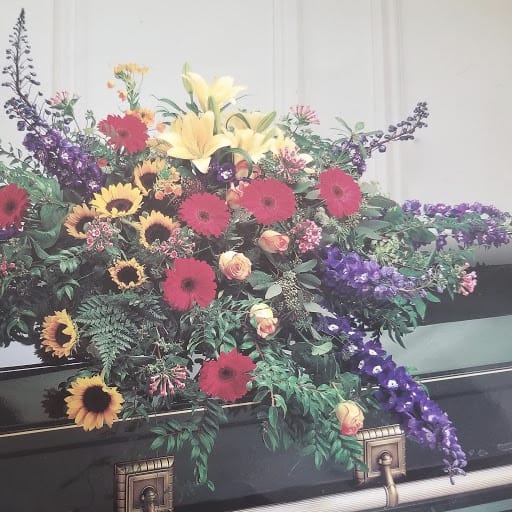 Garden of Grandeur Casket Spray - A tribute that communicates deep love. This dramatic casket spray is ideal for a full couch or closed casket, mixing beautiful blooms with interesting greenery. 