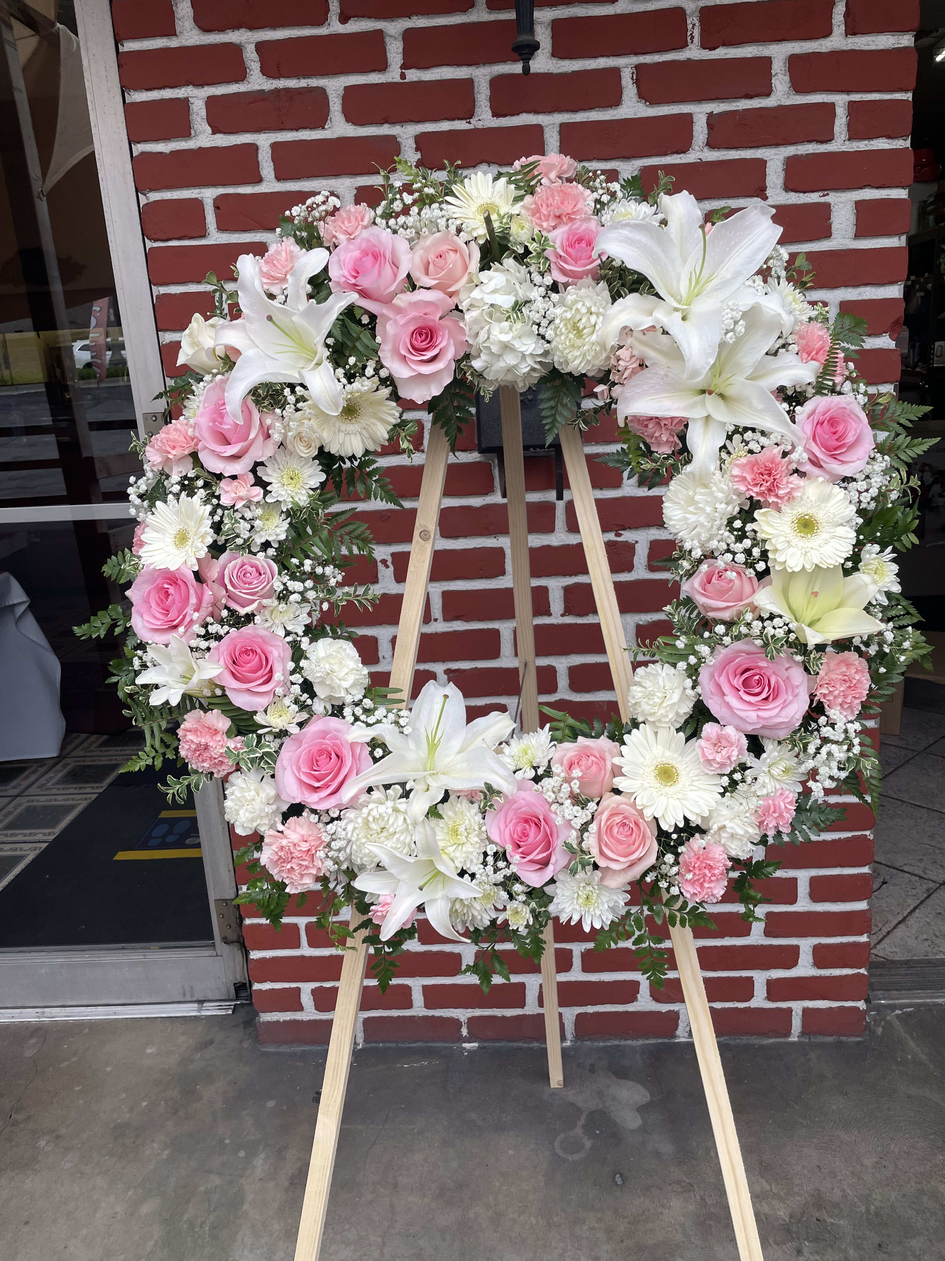 Pink rose & White lily Standing Wreath Pink rose & White lily Standing Wreath - The memories shared with a loved one can help bring serenity after they are gone. Our standing wreath in pink is a lovely way to celebrate those moments. Expertly crafted by our local florists with graceful pink and white blooms for a lush, full presentation, this traditional funeral arrangement is a beautiful way to honor their life. Standing wreath arrangement with pink roses, carnations and limonium; white football mums and daisy poms; accented with baby’s breath and soft, lush greenery