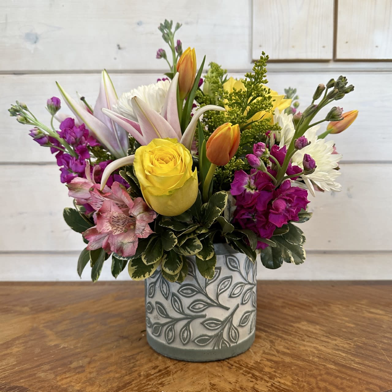 Happy Day Bouquet  - Yellow roses, stargazer lily, magenta stock, white chrysanthemums, orange tulips, and pink alstroemeria arranged in a medium laurel leaf cement pot with solidago. Approximately 12in tall and 12 in wide.  
